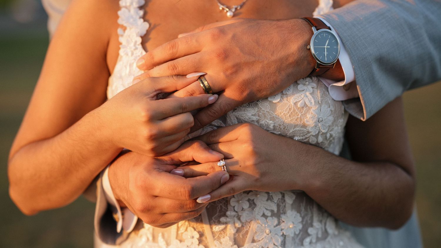 Close up of hands with wedding rings against white lace dress.