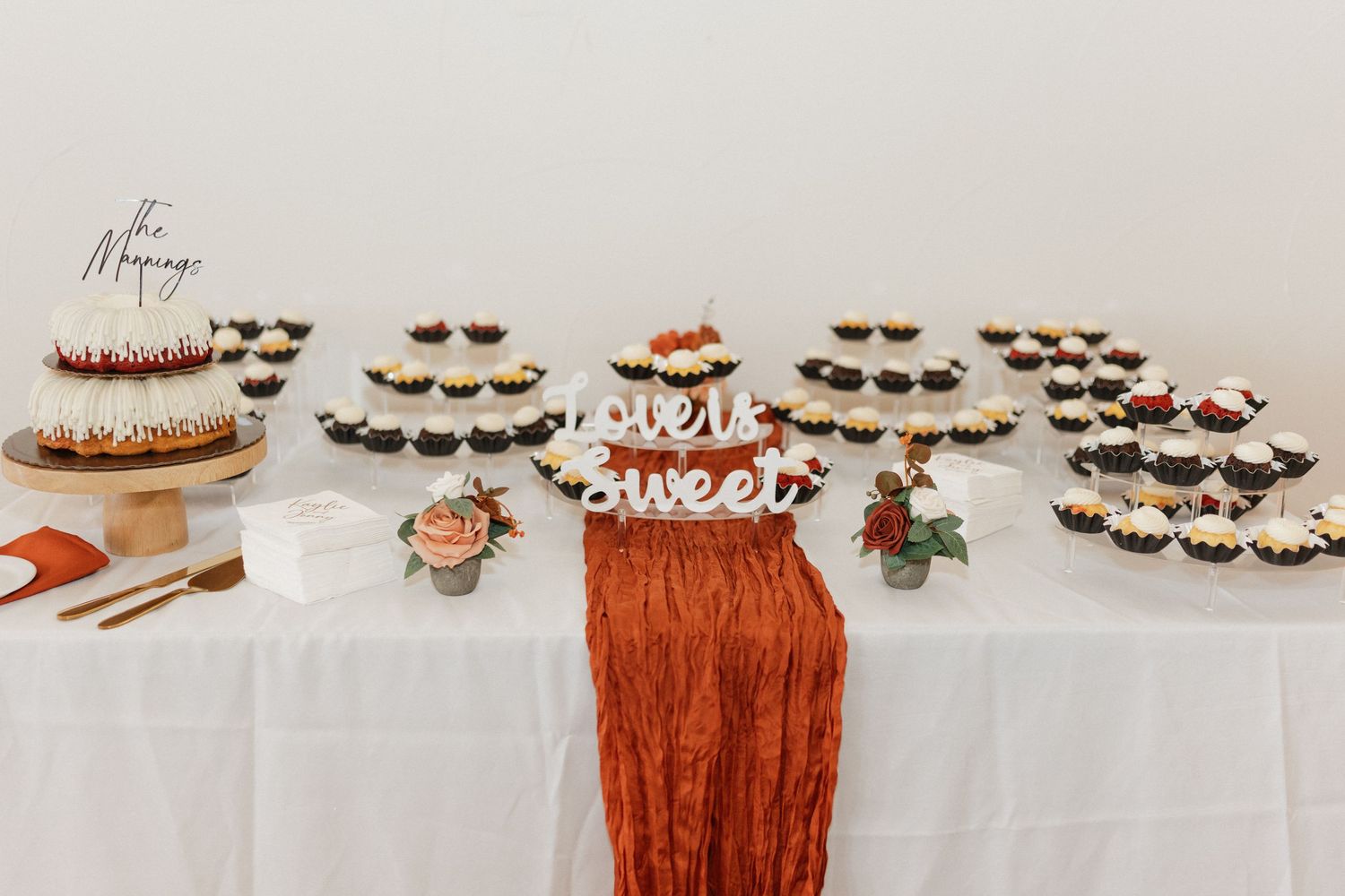 Dessert table display with cupcakes and treats decorated in terracotta and white colors.