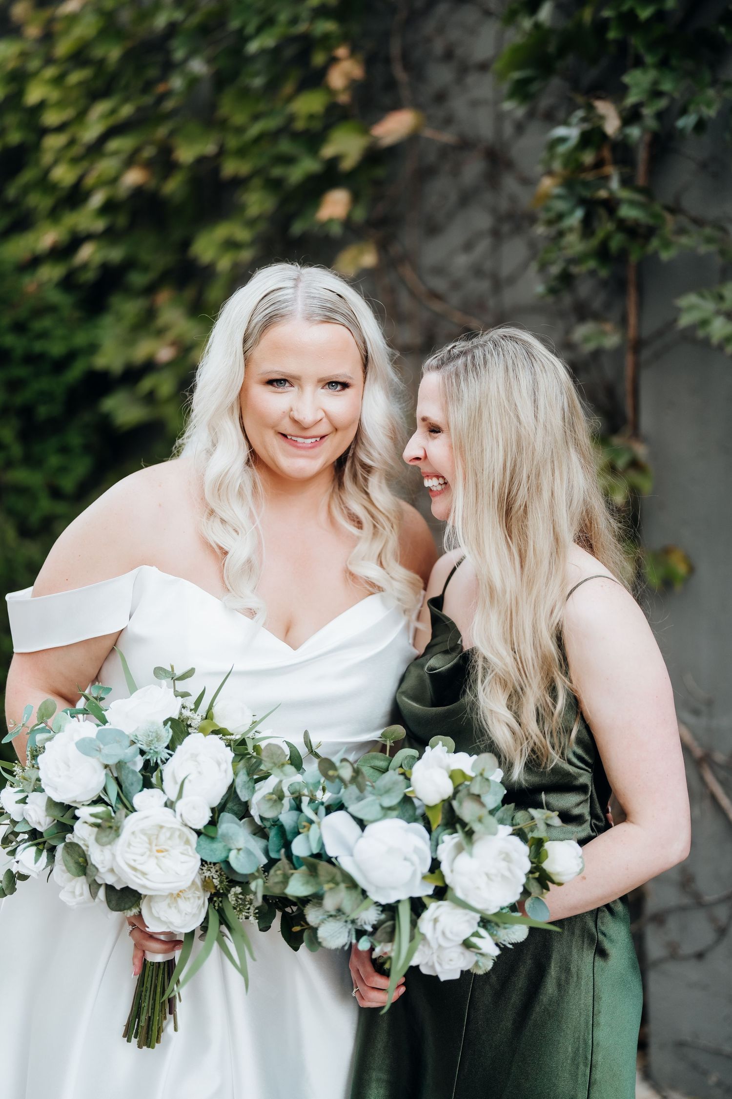 Bridesmaids in sage green dresses hold white bouquets while standing together outdoors.