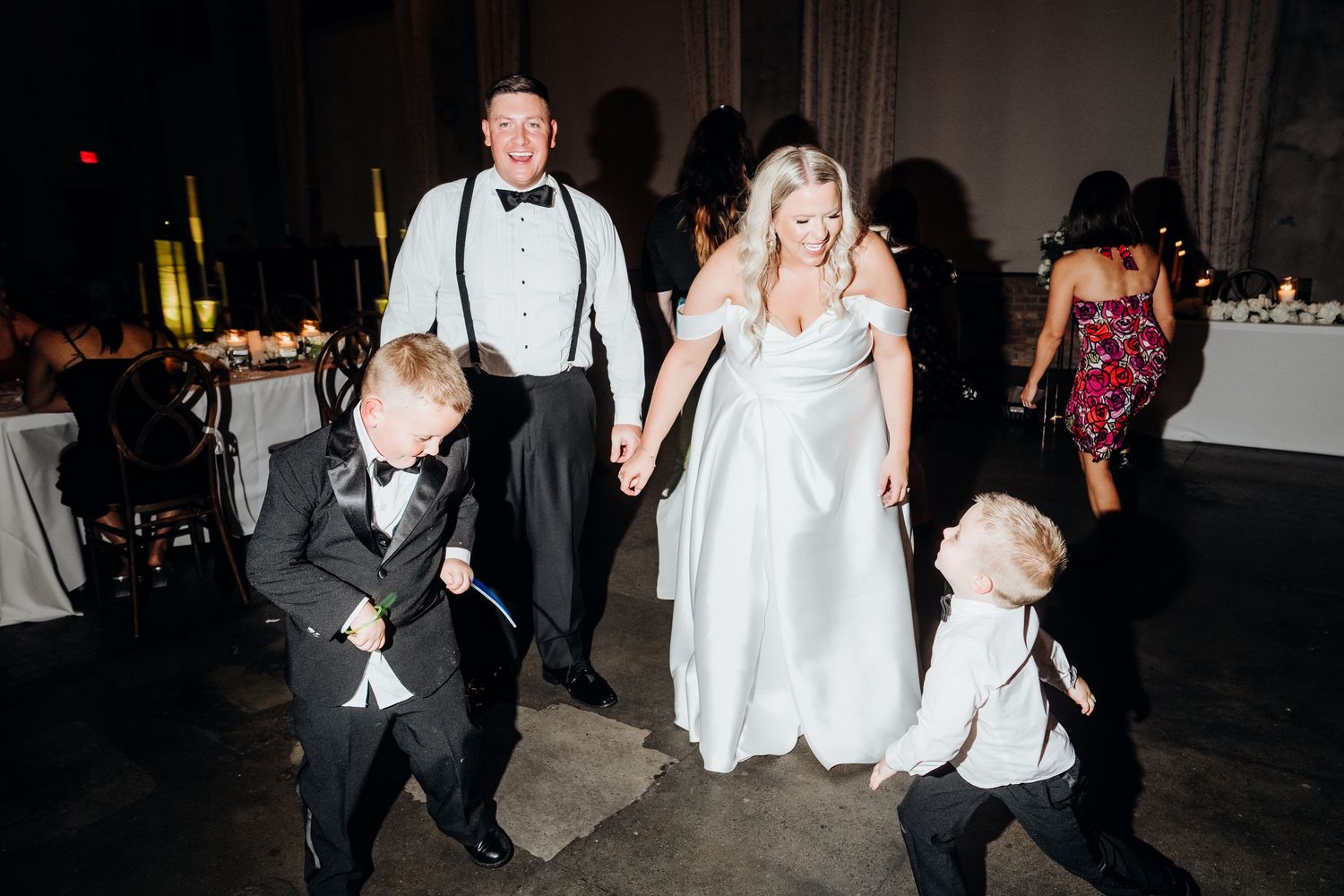 Wedding reception party dancing in dimly lit venue with festive atmosphere.
