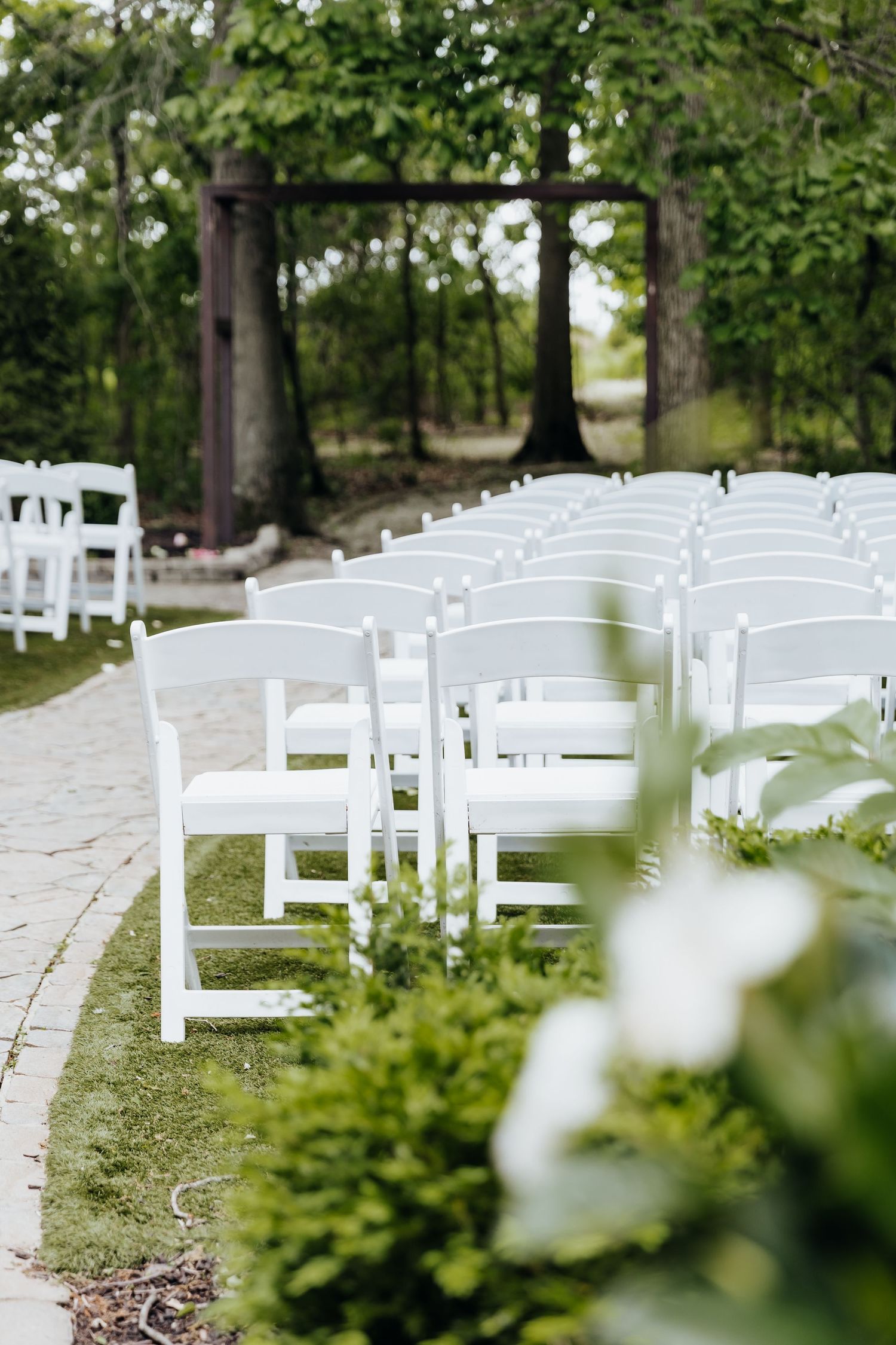 Rows of white folding chairs set up for an outdoor wedding ceremony with a rustic wooden arch in the background.