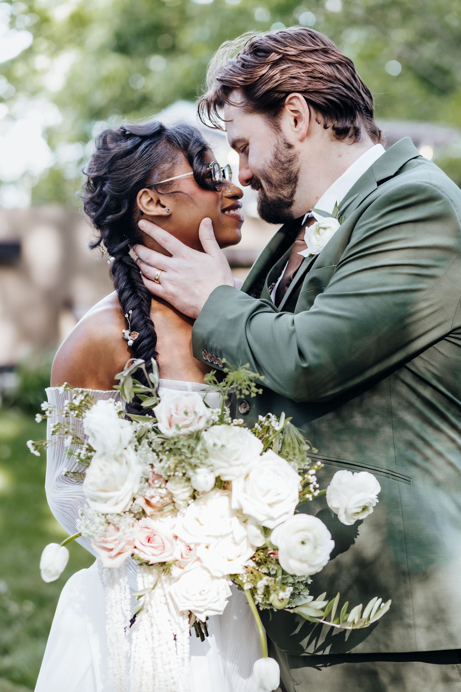 Romantic wedding couple embraces while holding elegant white and blush floral bouquet.