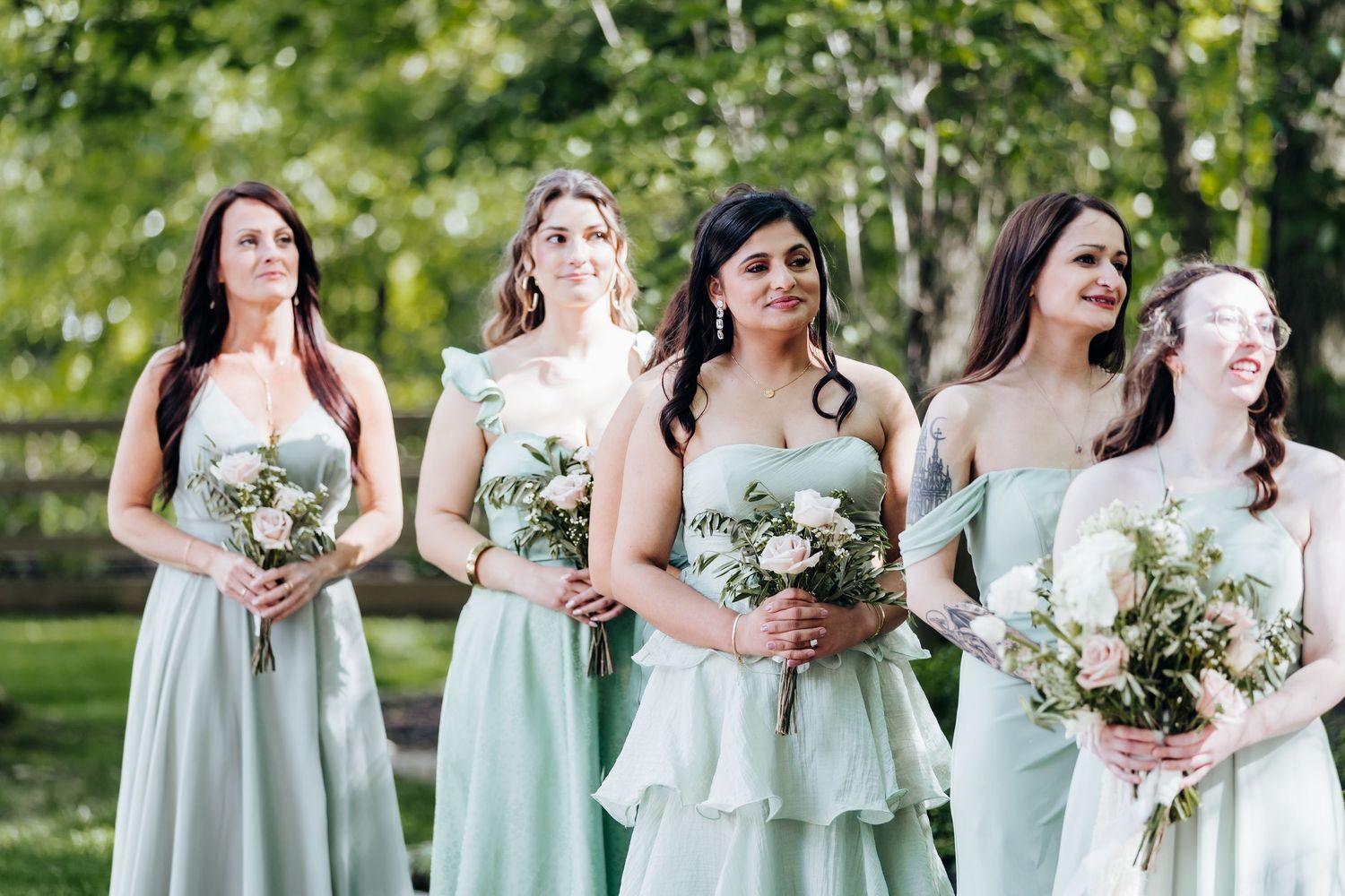 Bridesmaids in mint green dresses hold bouquets while posing together outdoors.