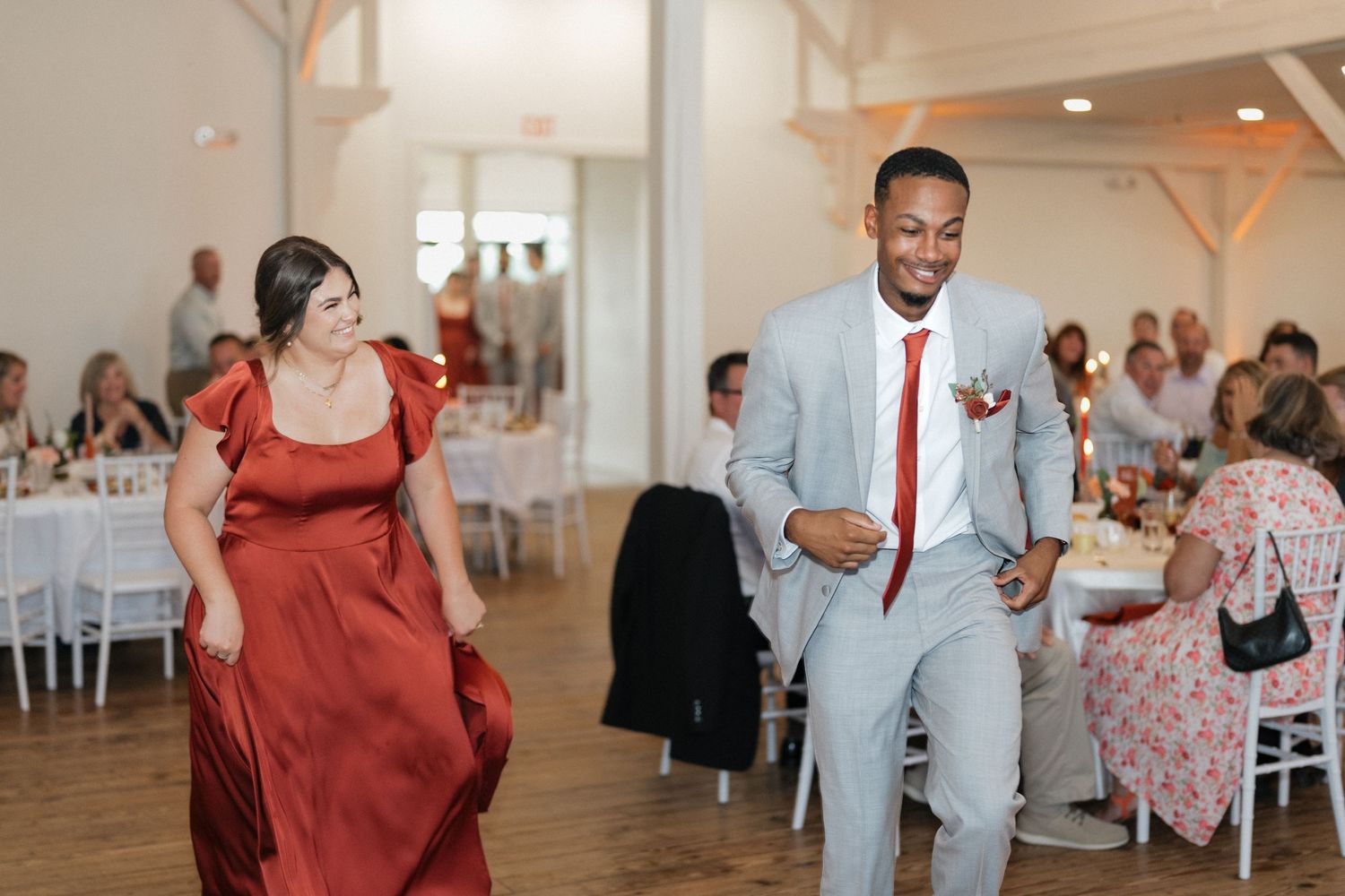 Wedding guests dancing and celebrating in a bright indoor venue with wooden beams and chandeliers.
