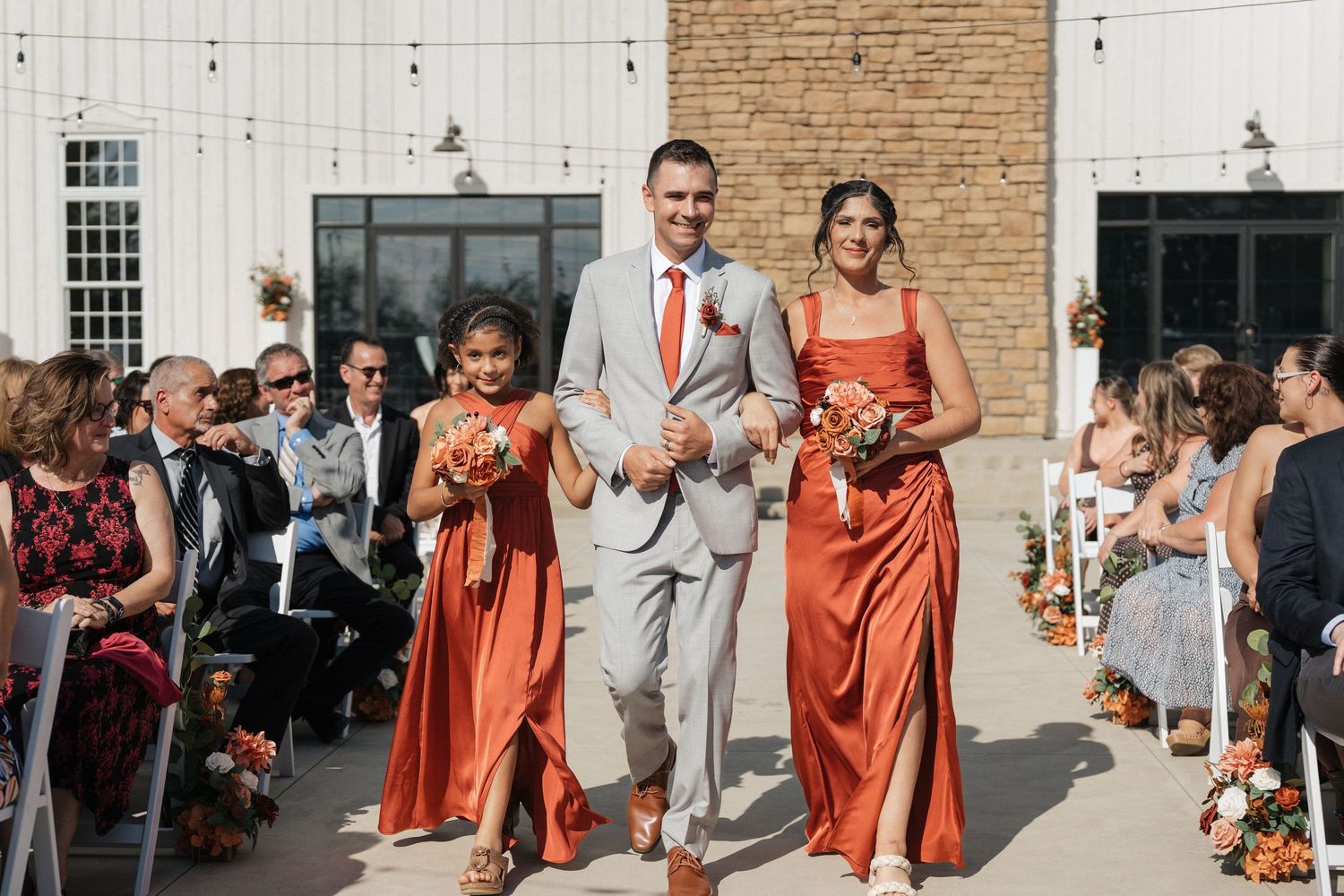 Wedding party walking and celebrating outside a white and brick building.