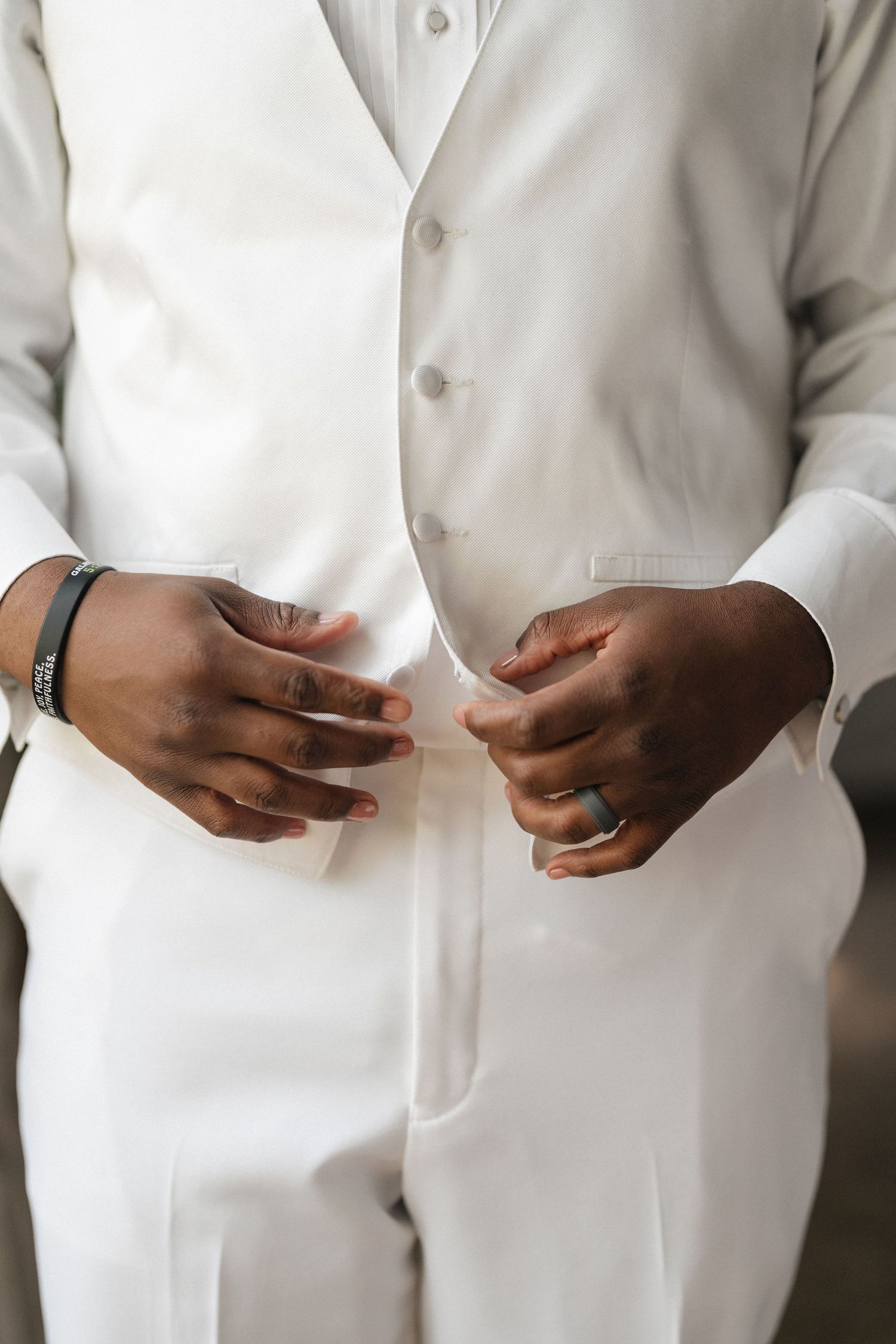 Close-up view of hands holding wedding rings against white formal attire.
