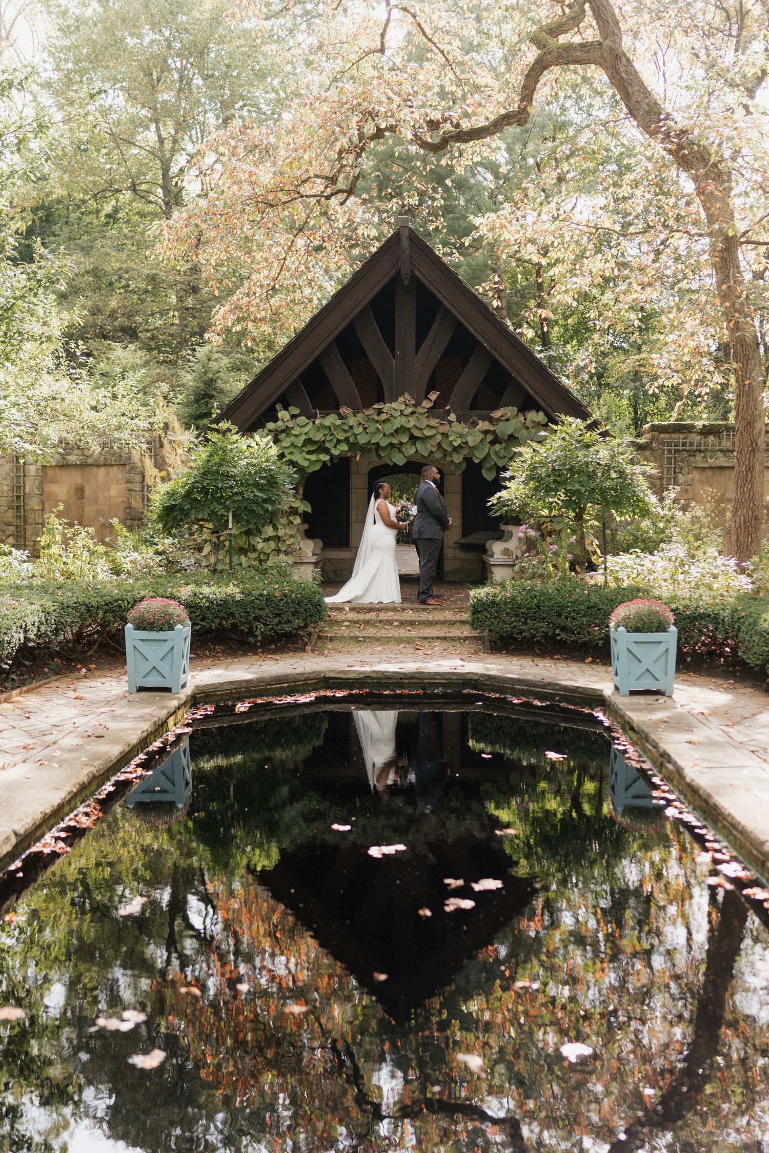 Scenic garden wedding venue with a wooden gazebo and reflective pond surrounded by blooming trees.