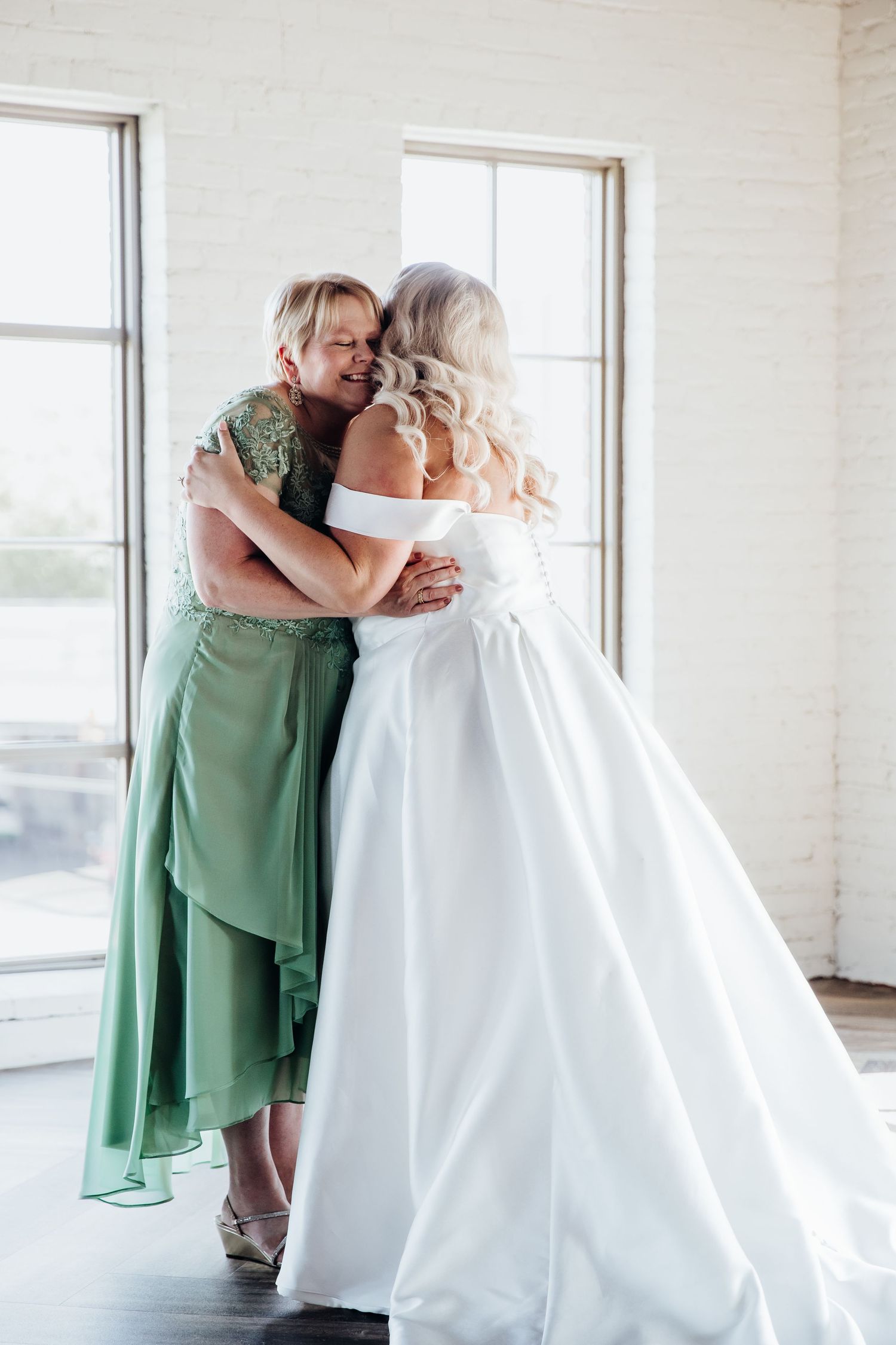 Emotional wedding moment with bridesmaids in green dresses embracing in a bright room.