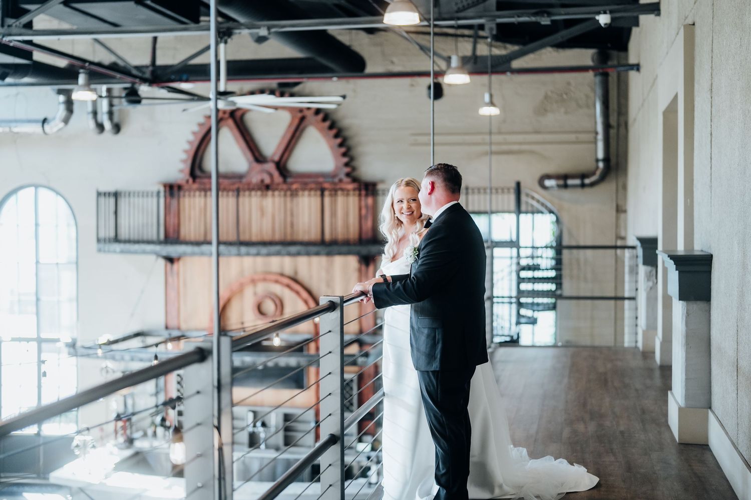 Wedding party members pose in an industrial-style venue with exposed ceiling and brick walls.