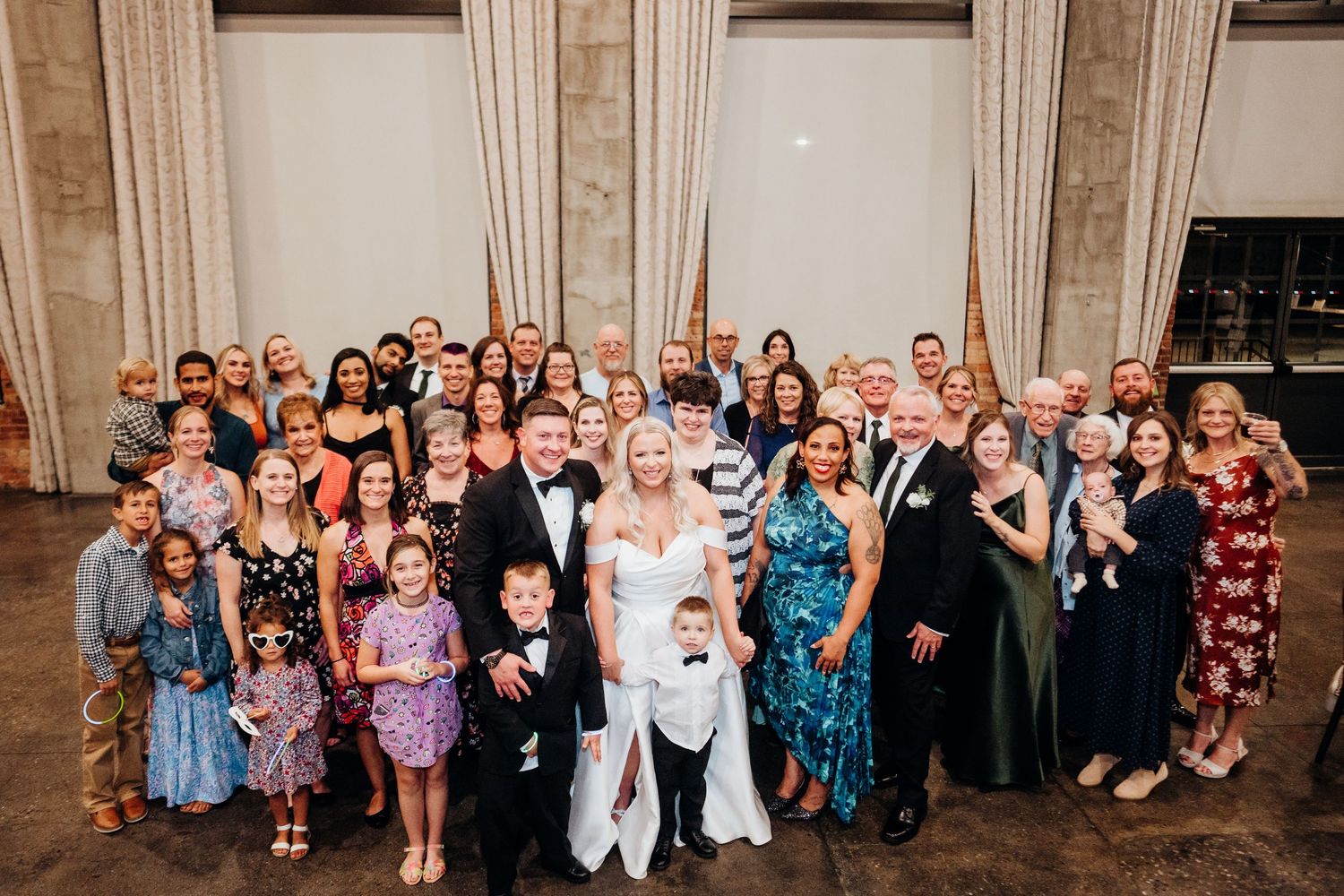 Large wedding group photo with guests gathered in an industrial-style venue.