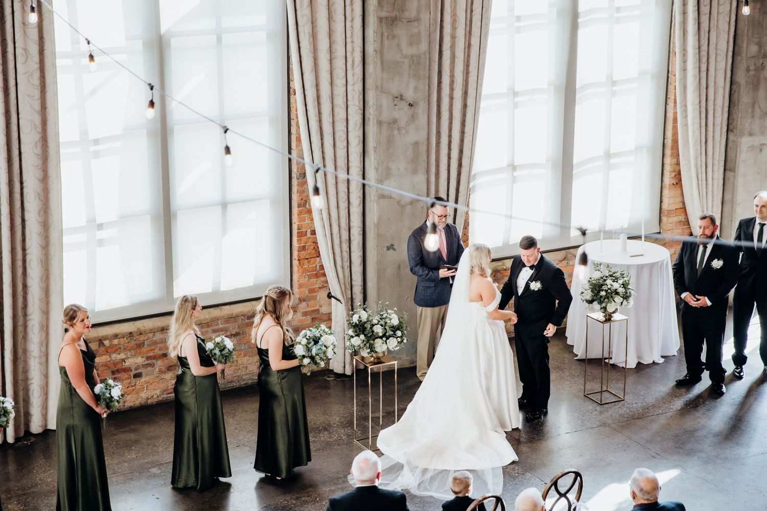 An overhead view of a wedding ceremony in a bright industrial venue with exposed brick walls.