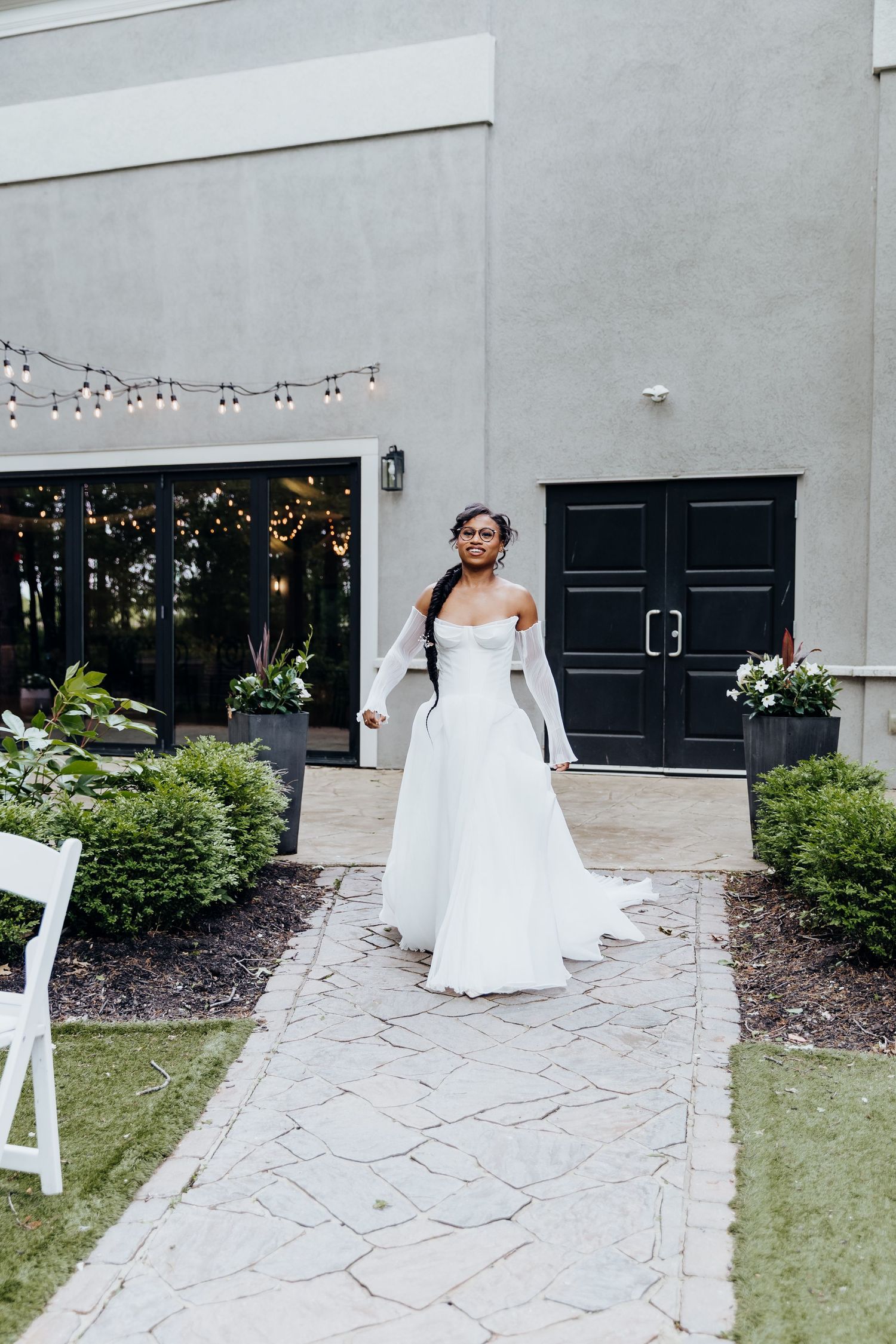 Wedding venue exterior with string lights and white decor against grey walls.
