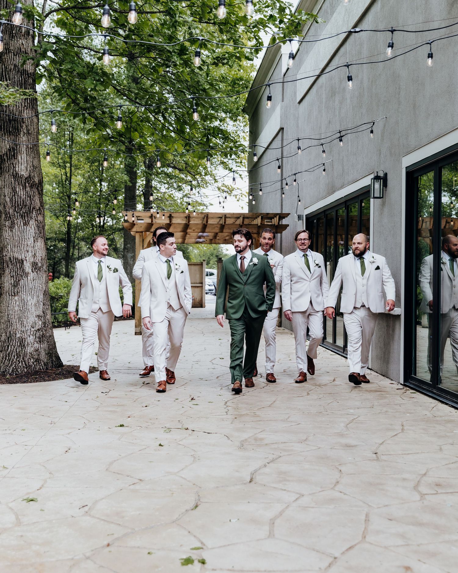 Wedding party walking together with groomsmen in white suits and one in green suit on stone pathway.