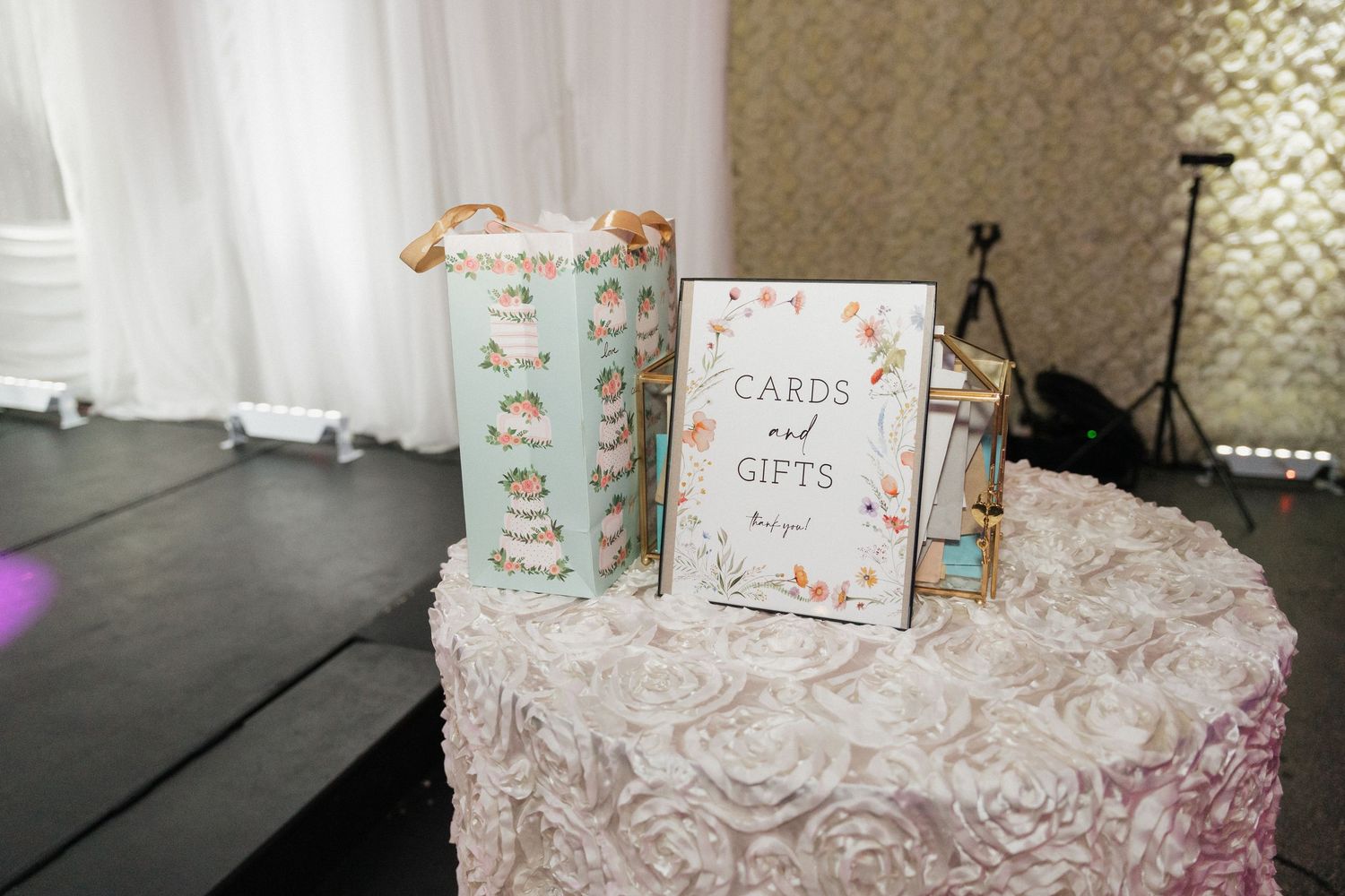 Elegant white wedding gift table with floral tablecloth and decorative signage.