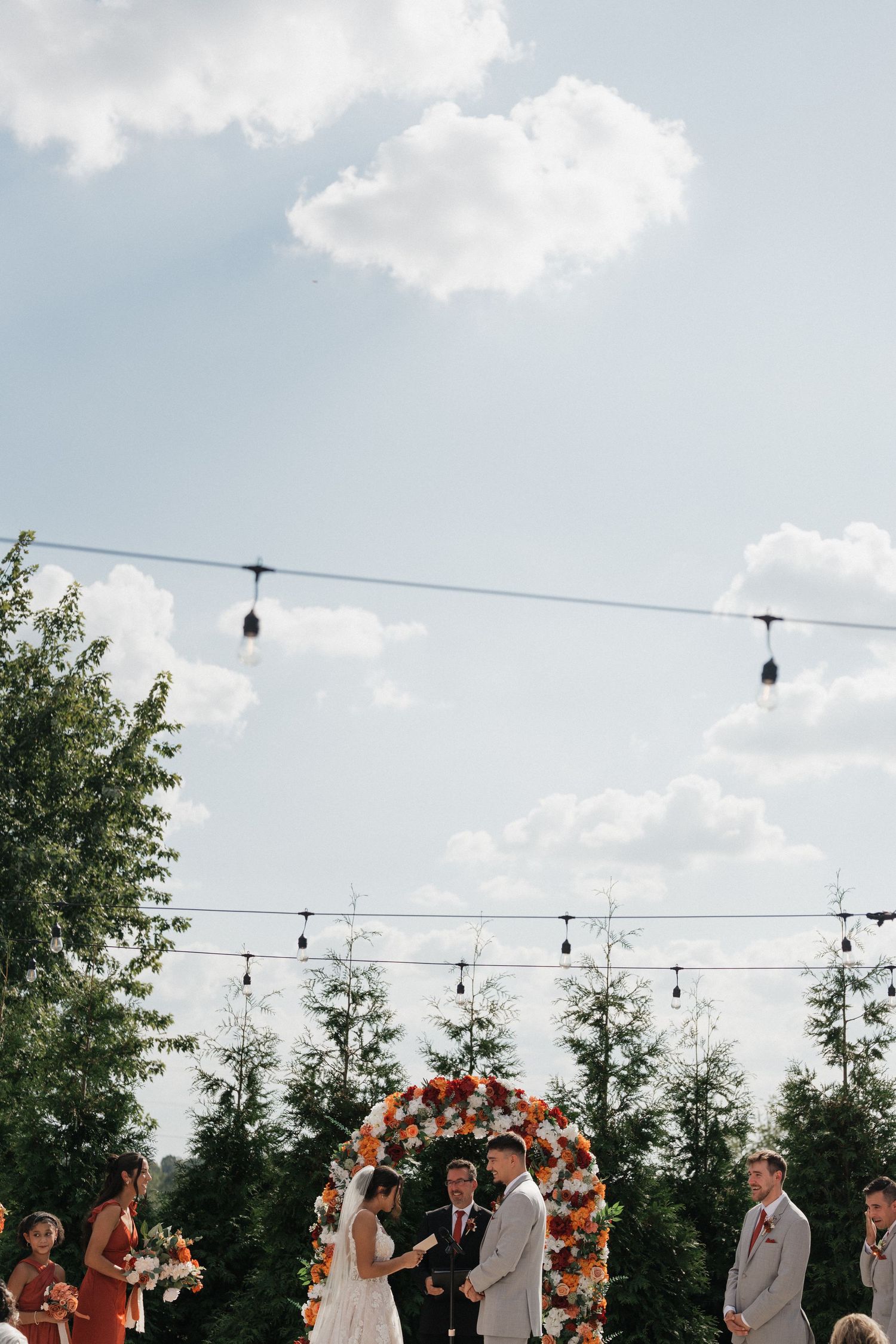 An outdoor wedding ceremony setup with string lights and floral arch against a blue sky.