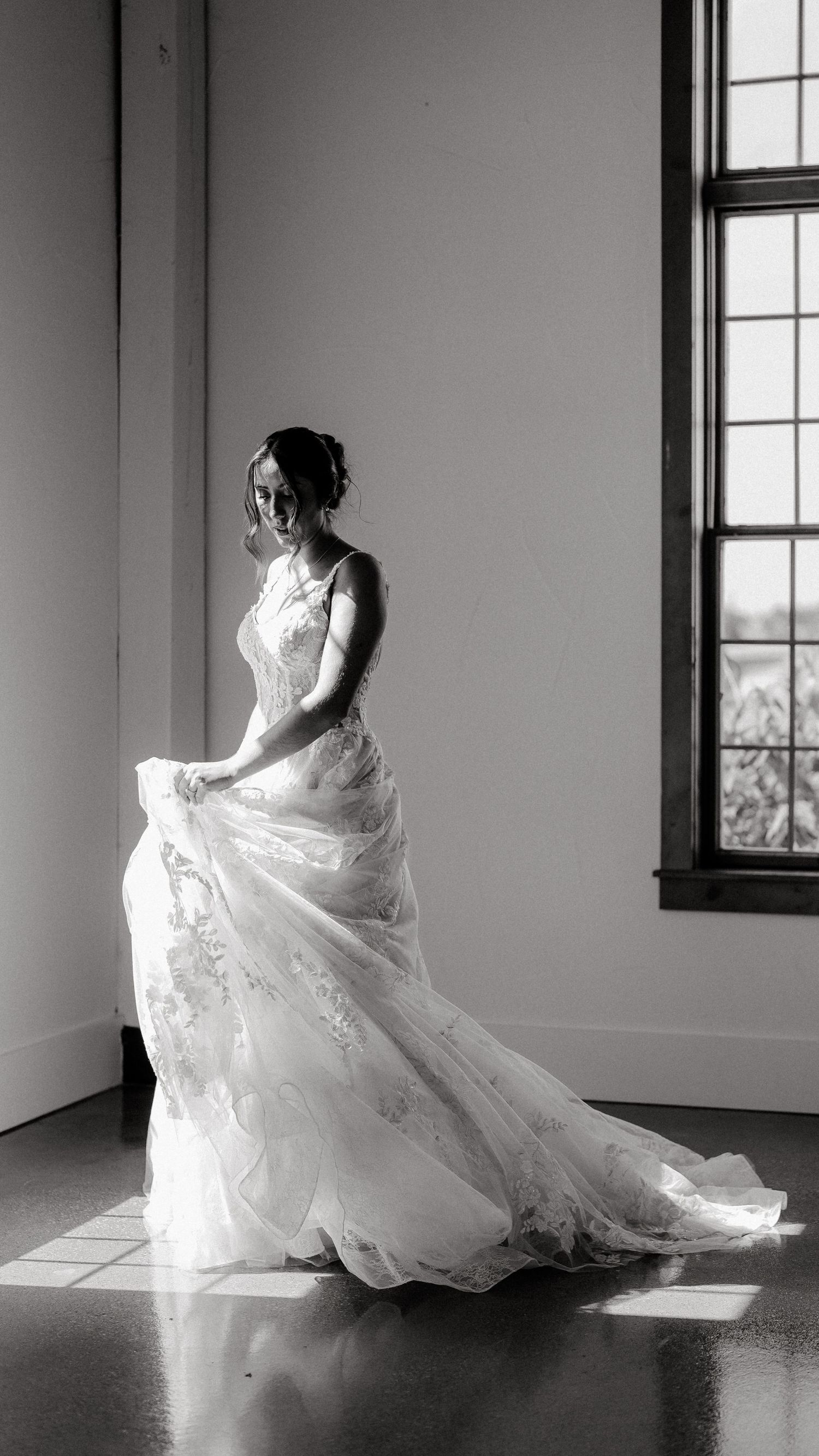 Bride in flowing white wedding gown twirls gracefully in sunlit room during bridal portraits.