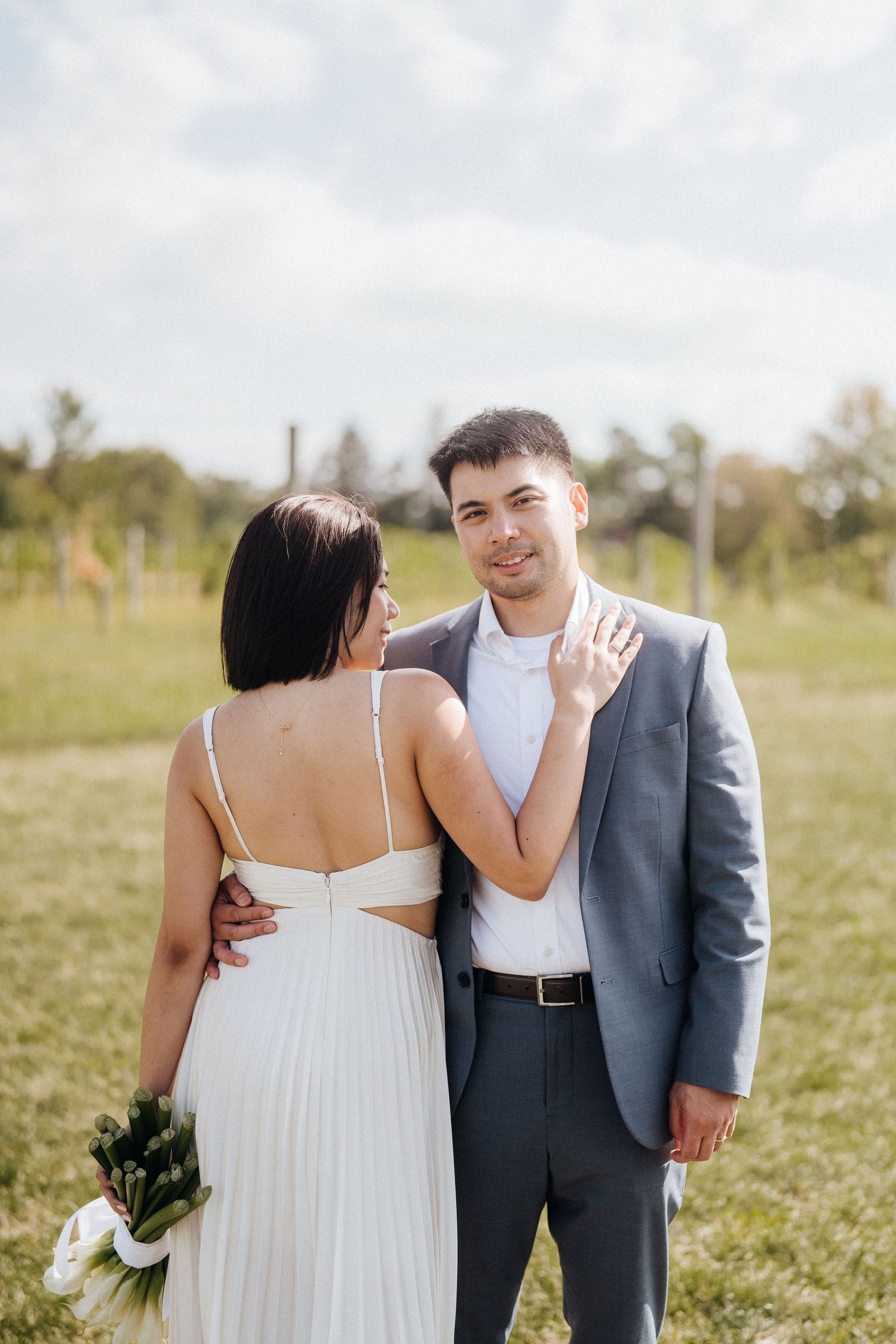 A couple in wedding attire shares an intimate moment in a green outdoor setting.