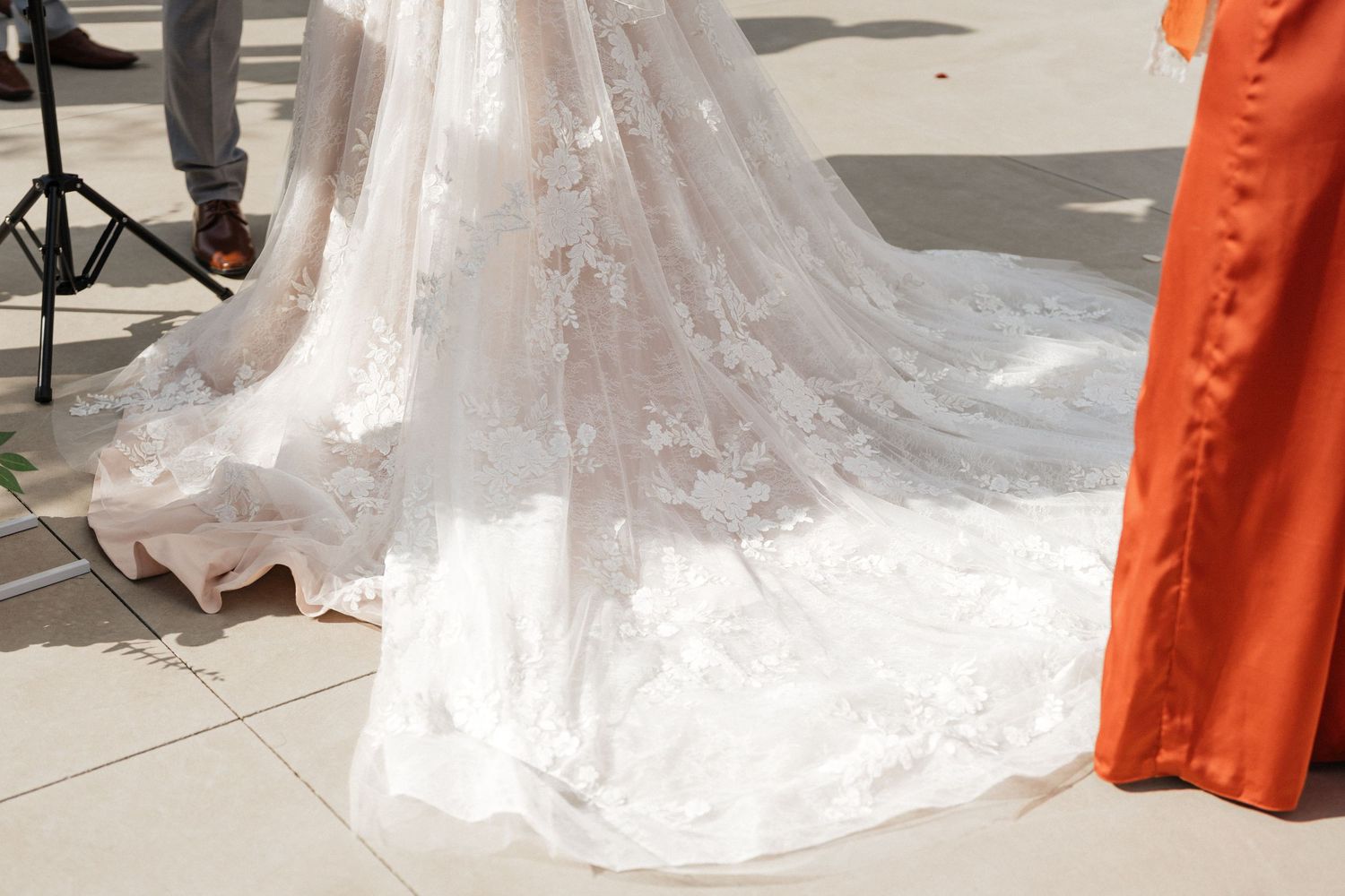 Wedding dress train trailing on concrete with orange bridesmaid dresses visible in frame.