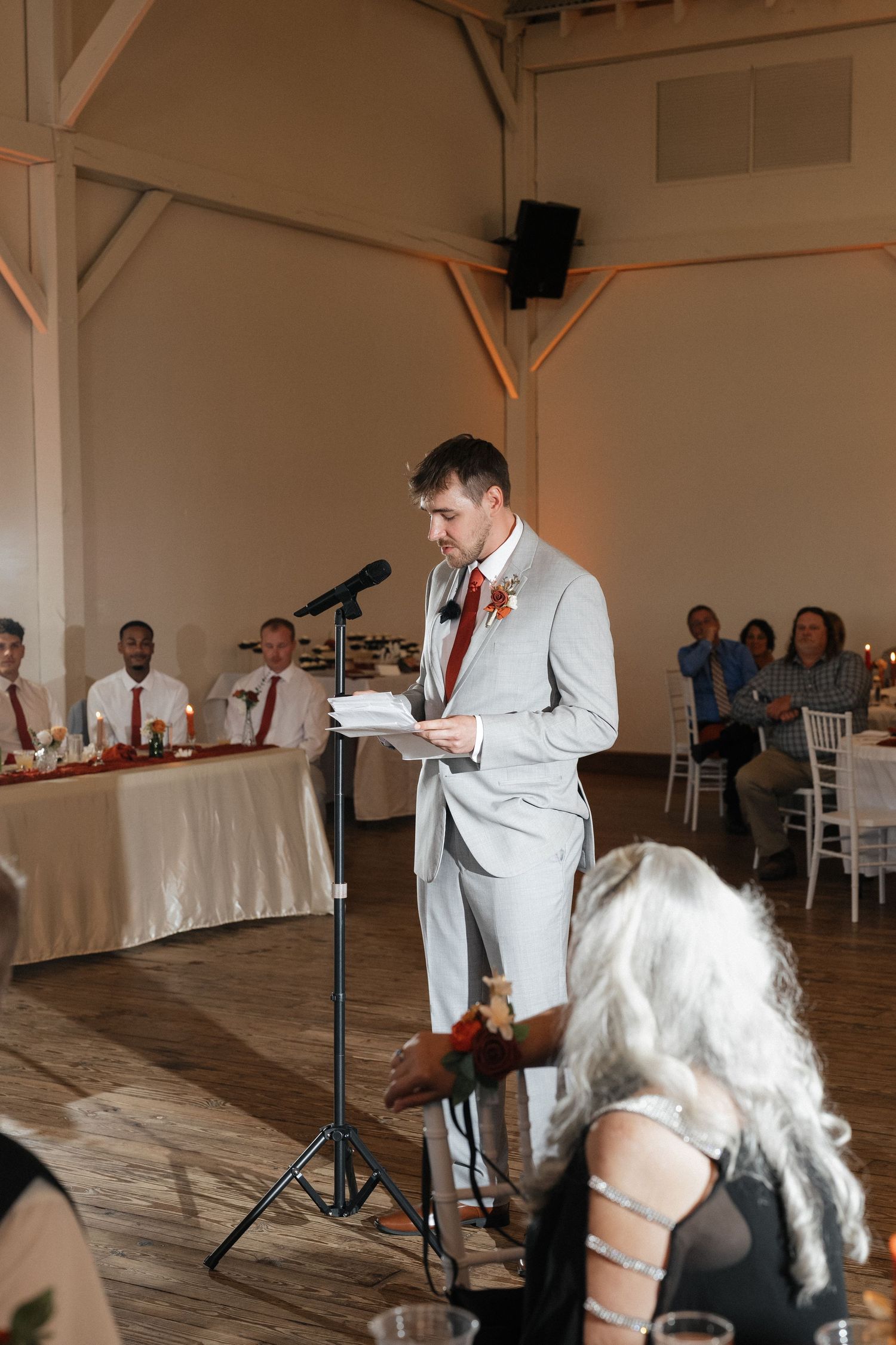 Wedding reception speeches in a rustic white barn venue with wooden floors and exposed beams.