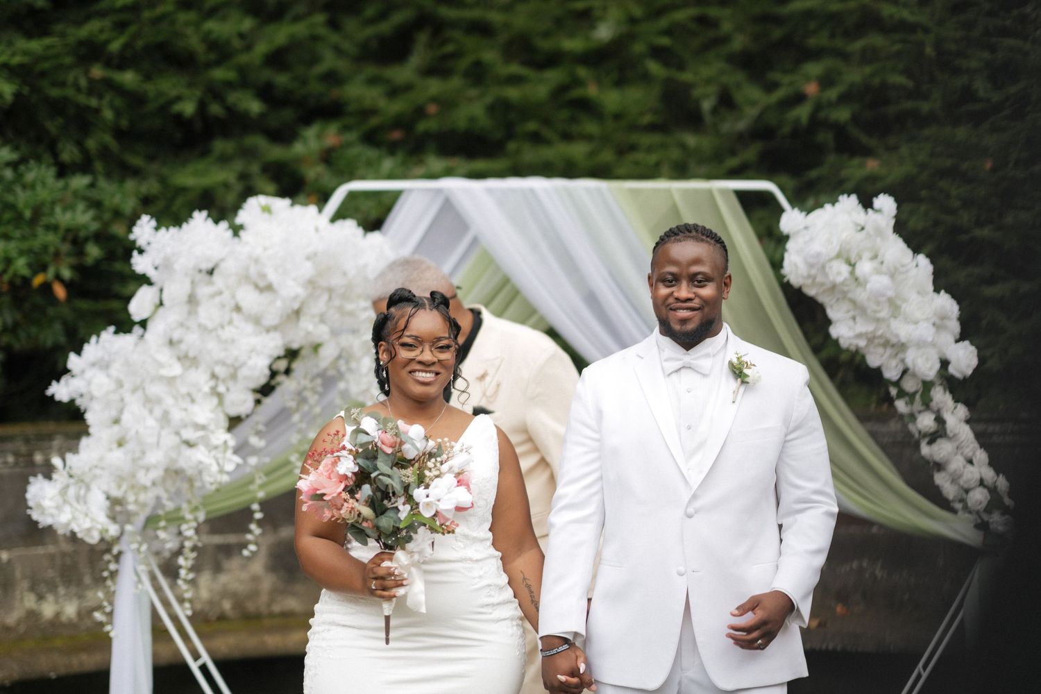 Elegant outdoor wedding ceremony setup with white floral arrangements and greenery backdrop.