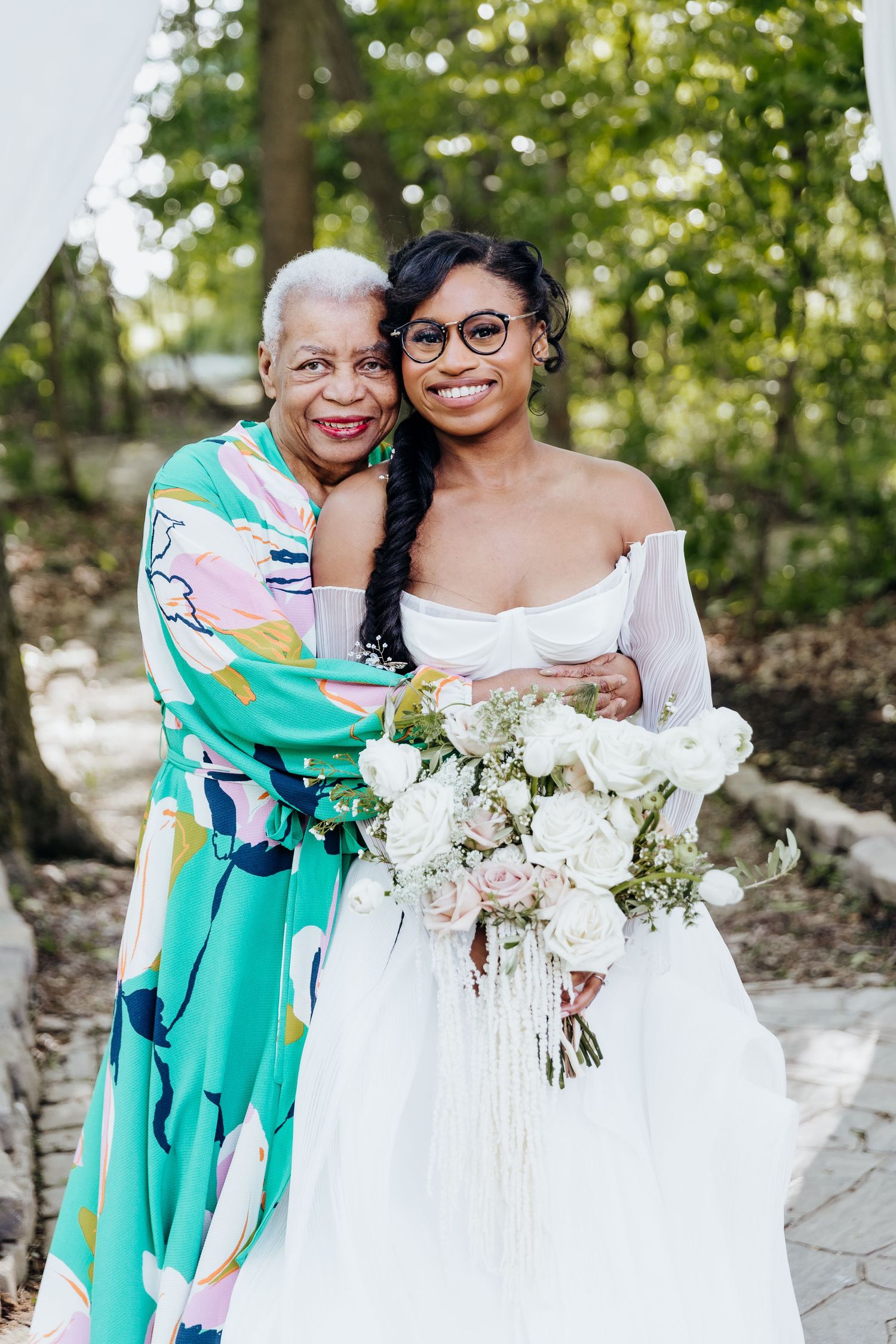 Wedding party members in turquoise floral dresses hold white bouquets during outdoor celebration.