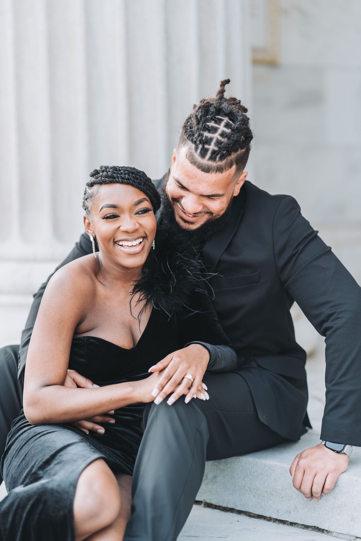 Elegant couple in black formal wear sharing a joyful moment on marble steps.