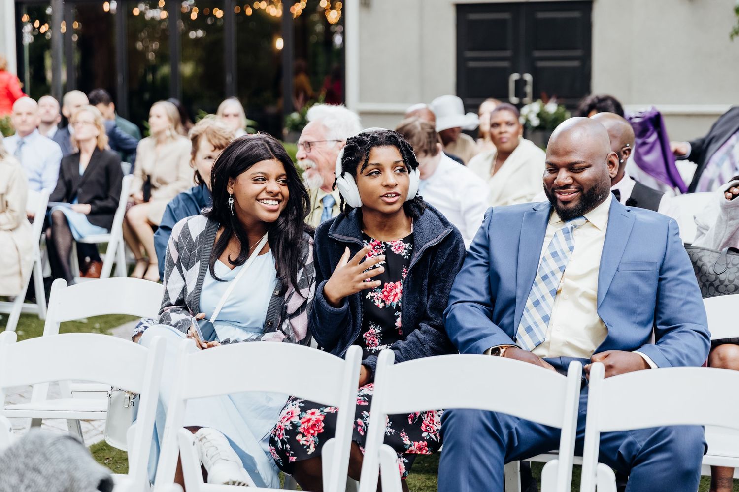 Wedding guests seated in white chairs at an outdoor ceremony venue.
