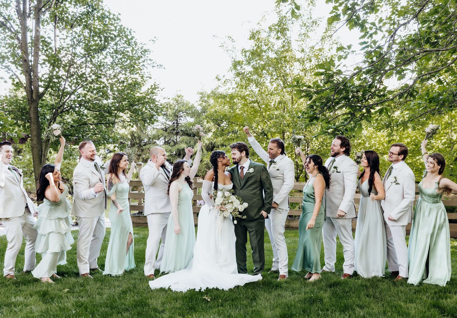 Wedding party in mint green dresses and white attire poses together on grassy lawn.