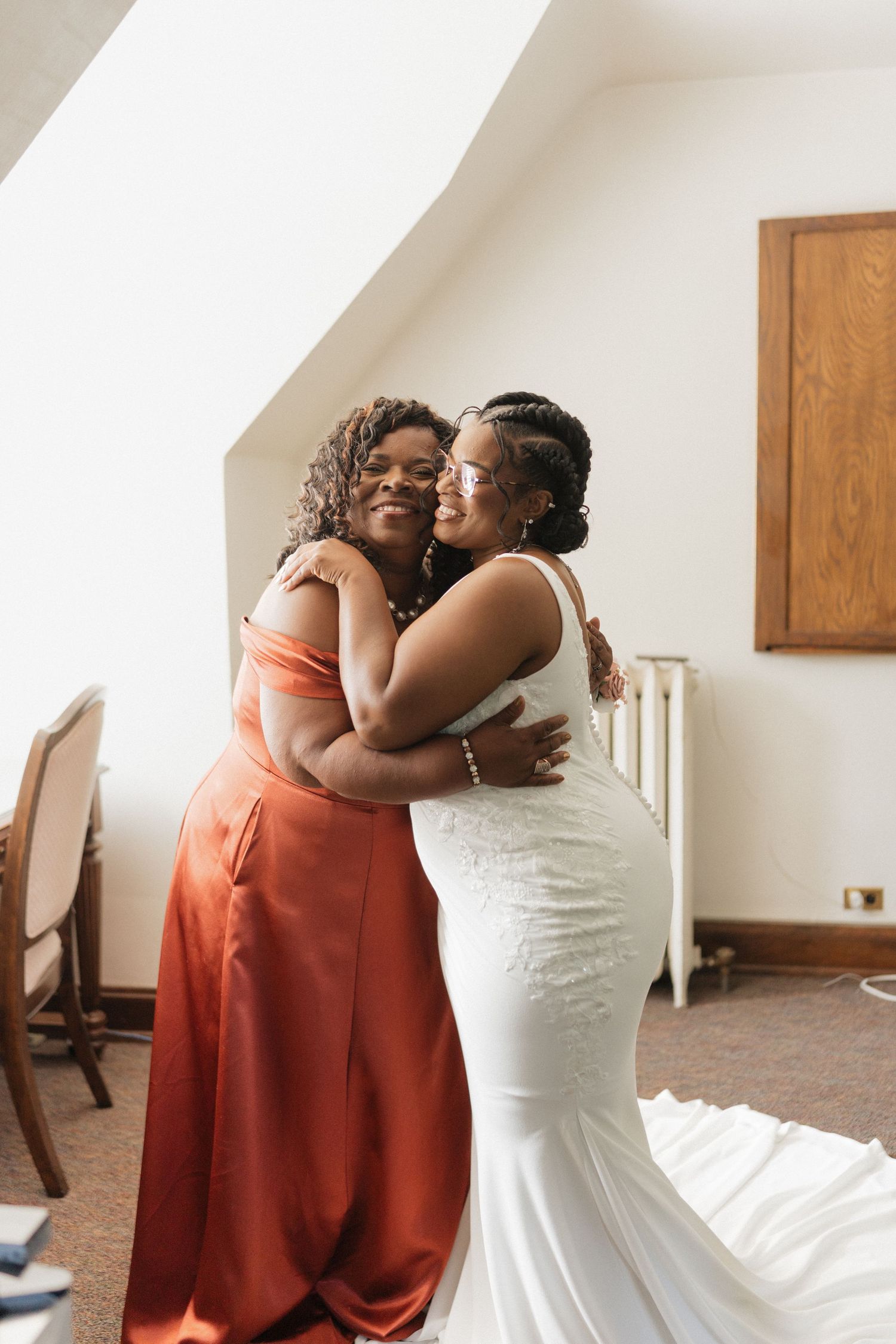 Two people share a joyful embrace, one wearing an elegant orange dress and the other in a stunning white wedding gown.