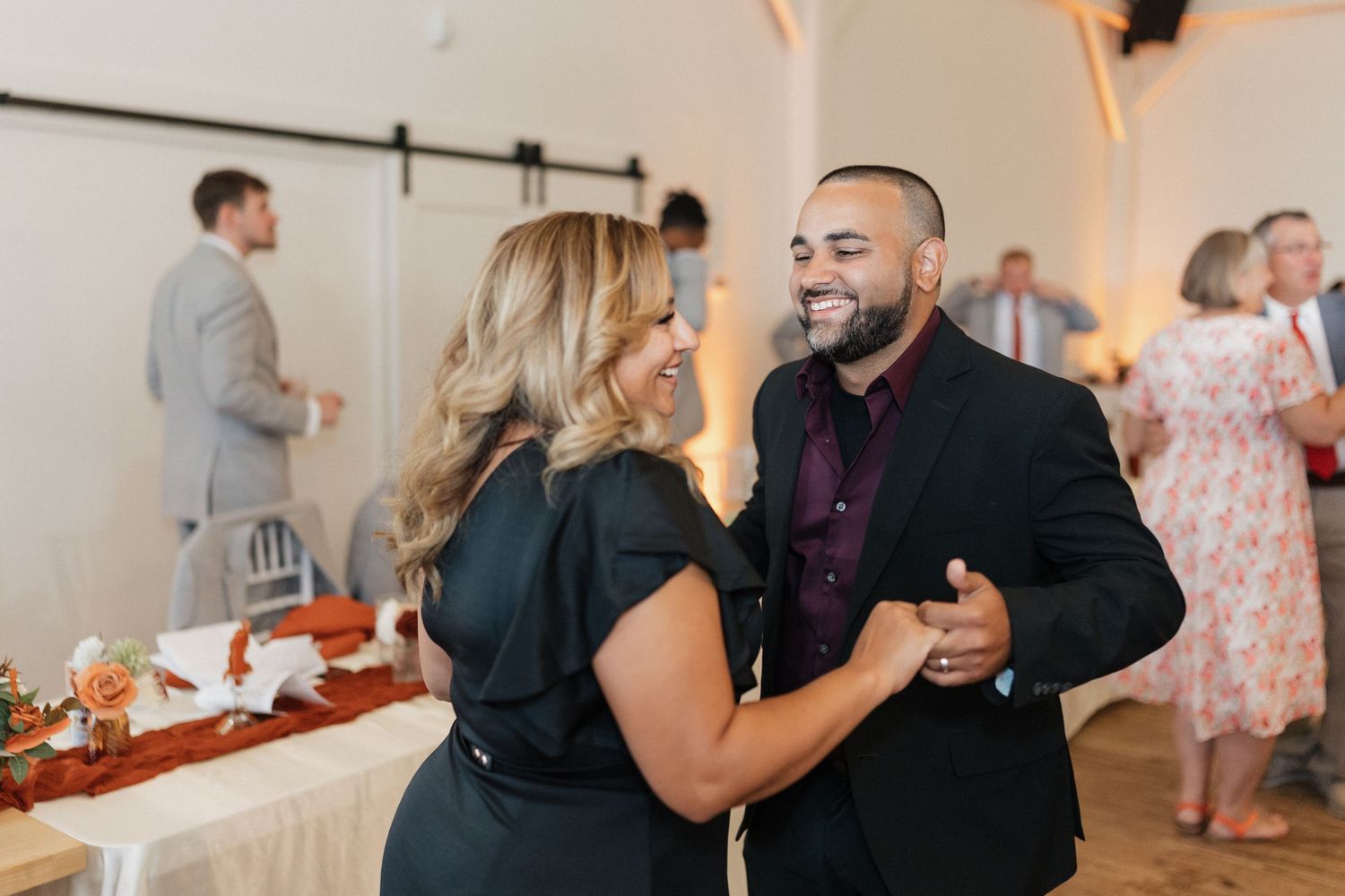 Wedding guests dancing and celebrating at an indoor reception with warm lighting.
