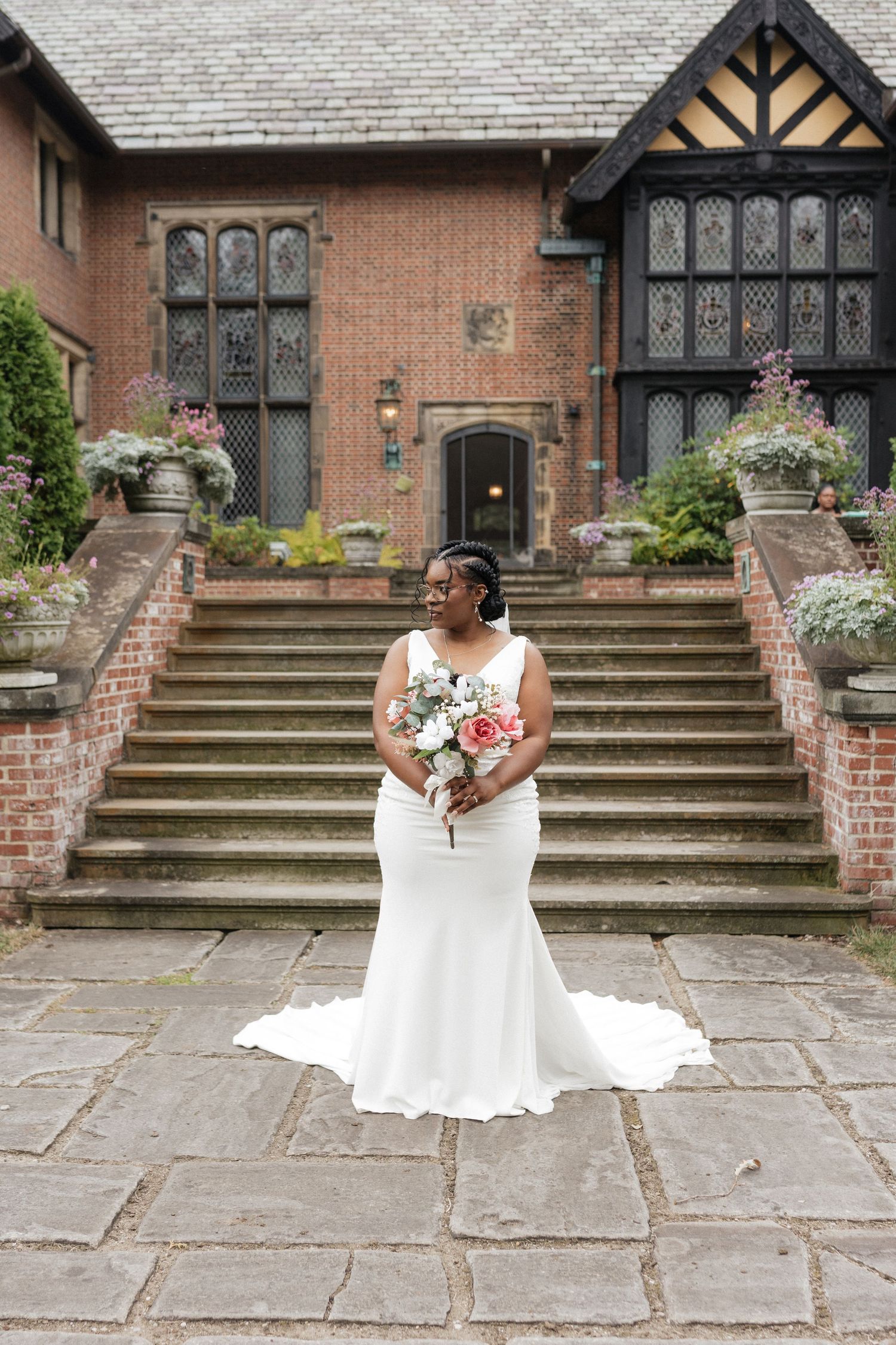 A beautiful white wedding dress flows across stone steps at a historic brick venue with Tudor-style architecture.