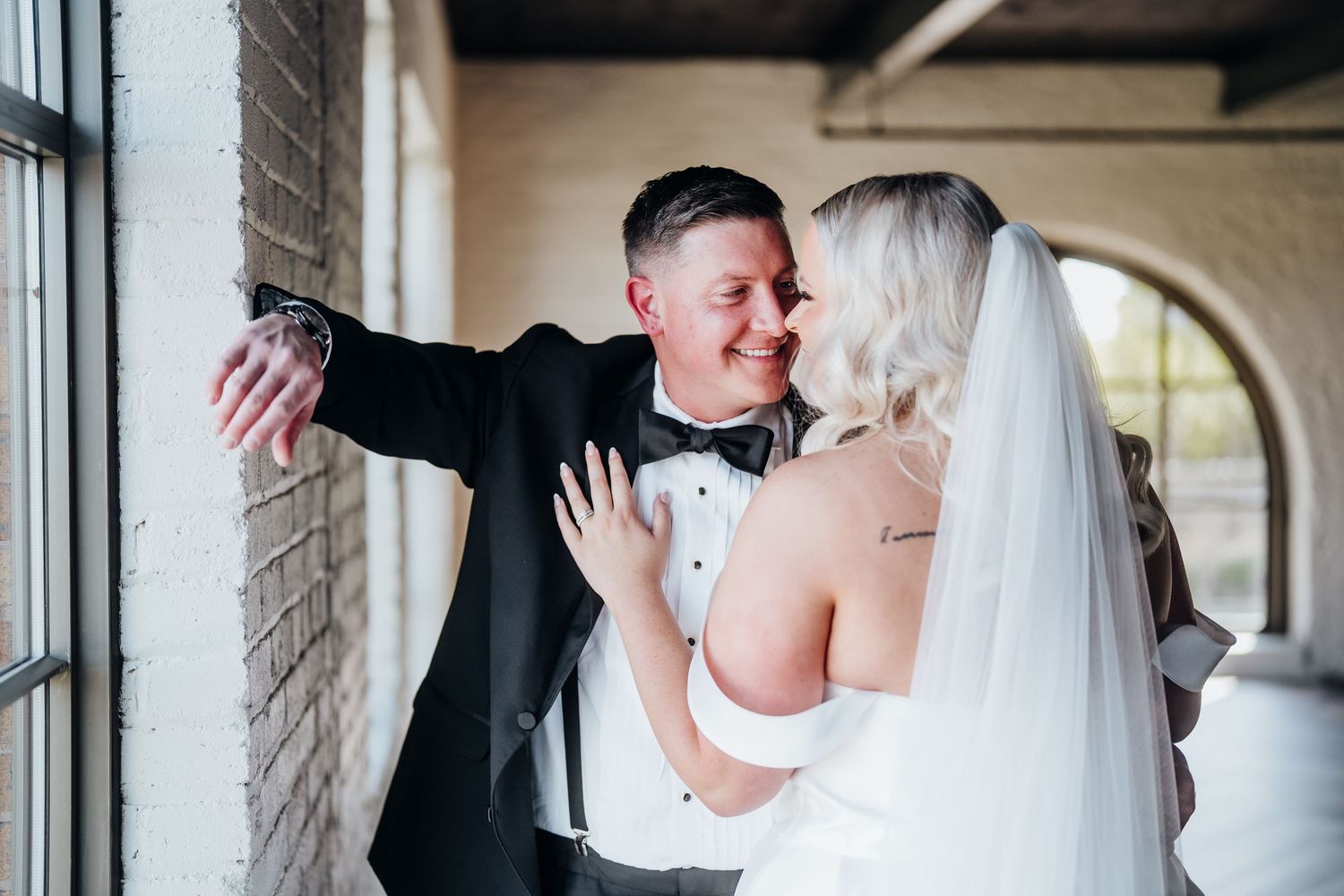 A romantic wedding couple shares a tender kiss in an elegant venue with white columns.