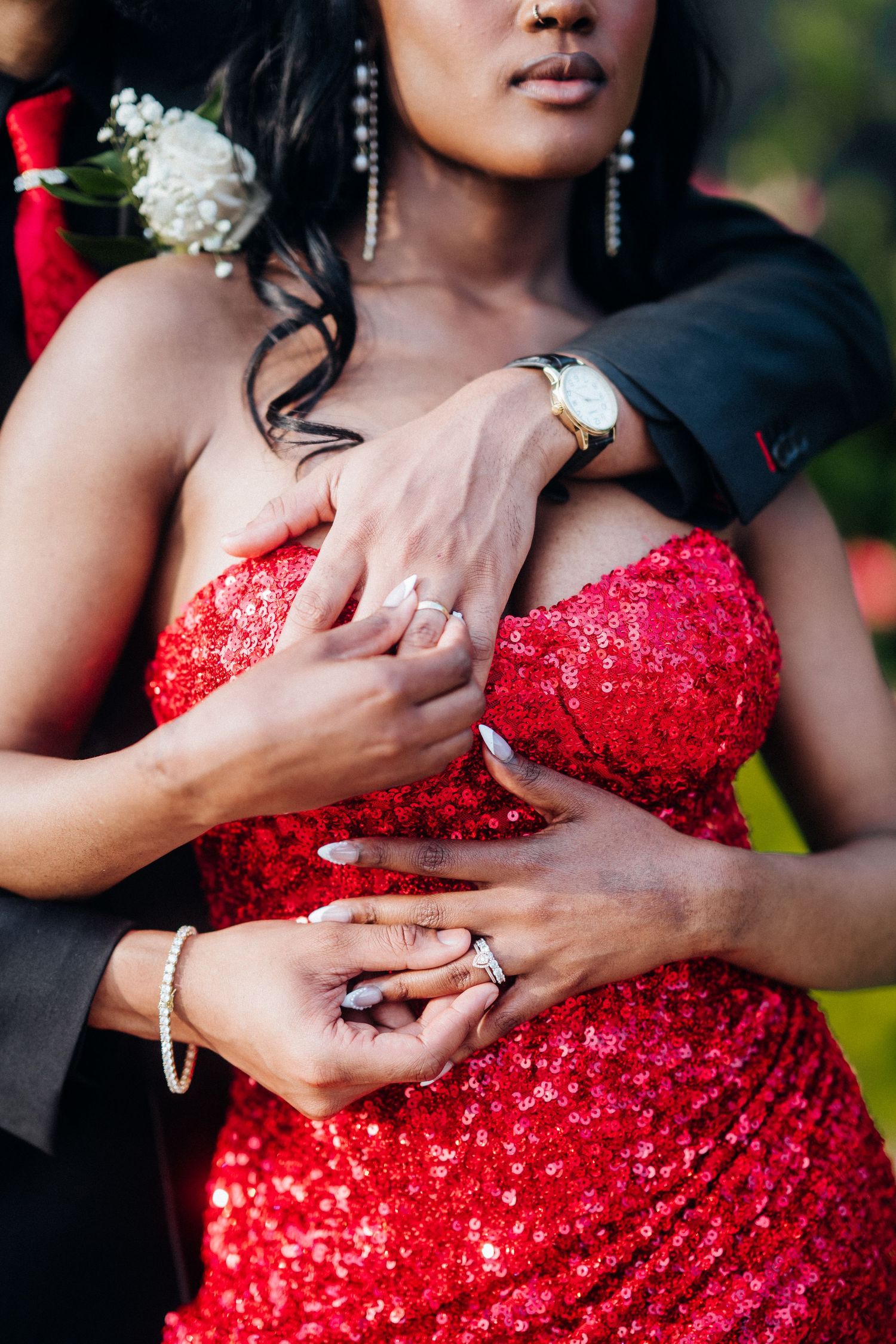 Detail shot of hands showing wedding rings against a sparkly red dress.