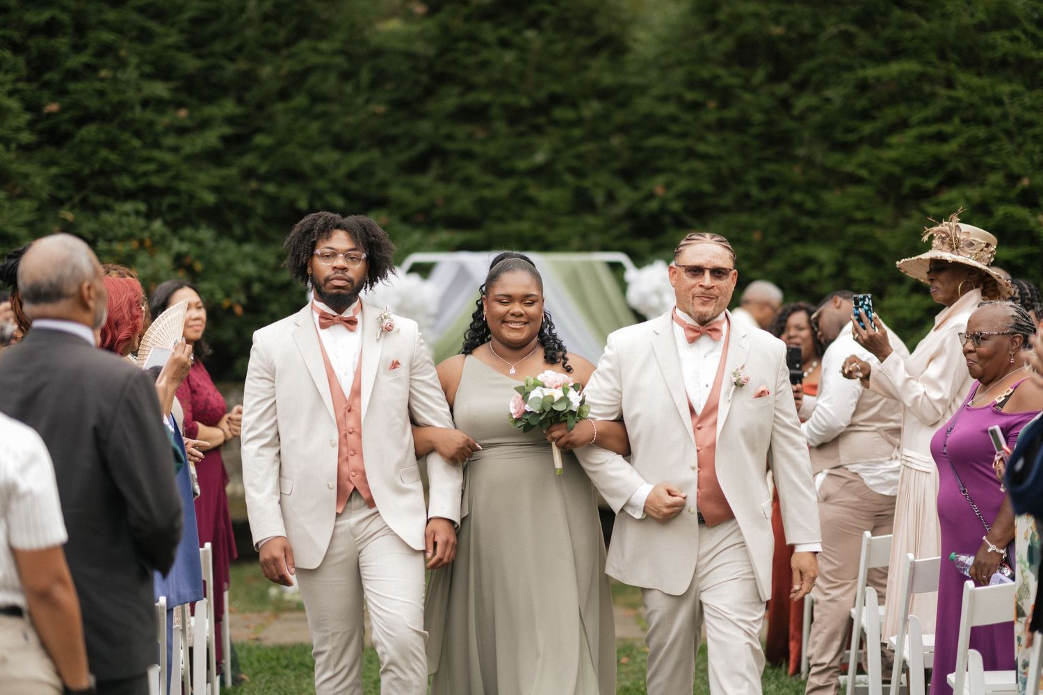 Wedding party members in white and beige attire walk together during outdoor celebration.
