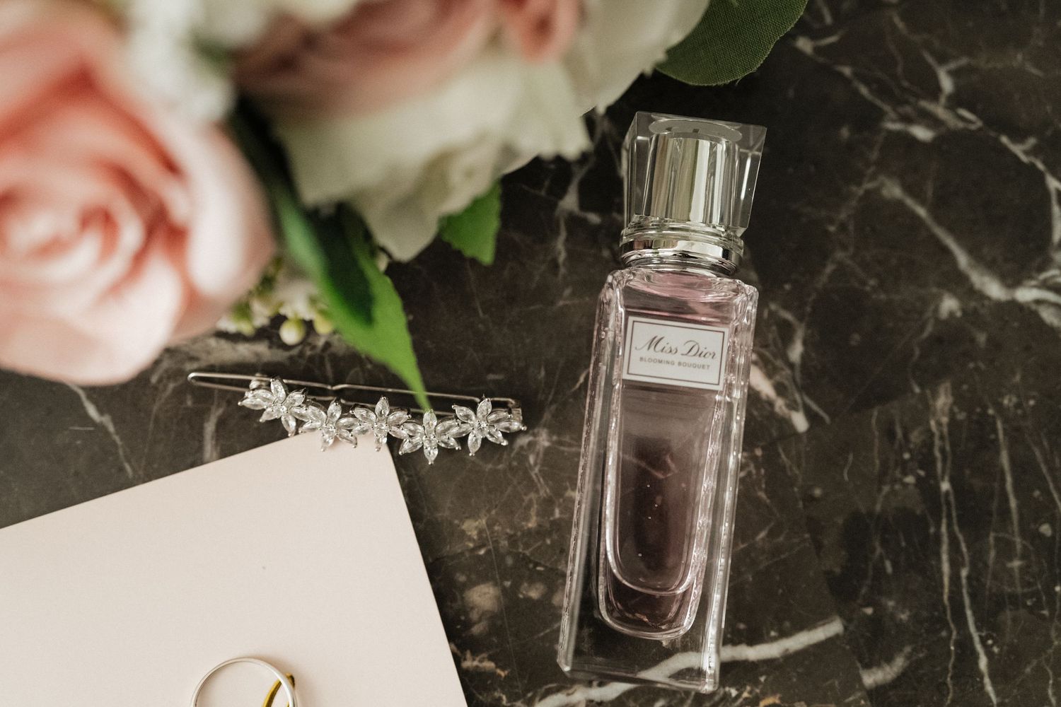 Elegant perfume bottle and pink roses arranged on dark marble surface with soft romantic lighting.