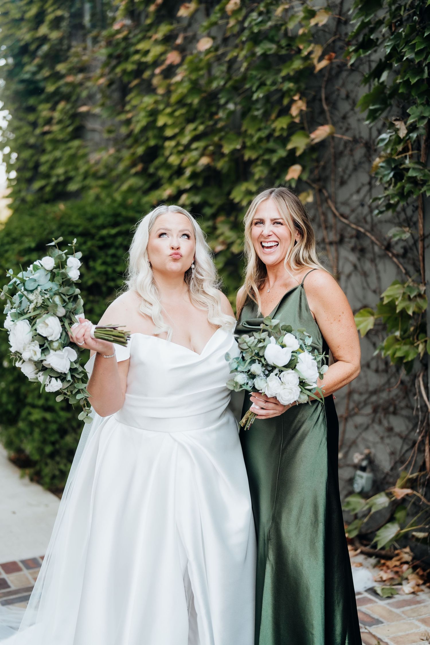 Wedding party in white and sage green dresses sharing candid laughs outdoors.
