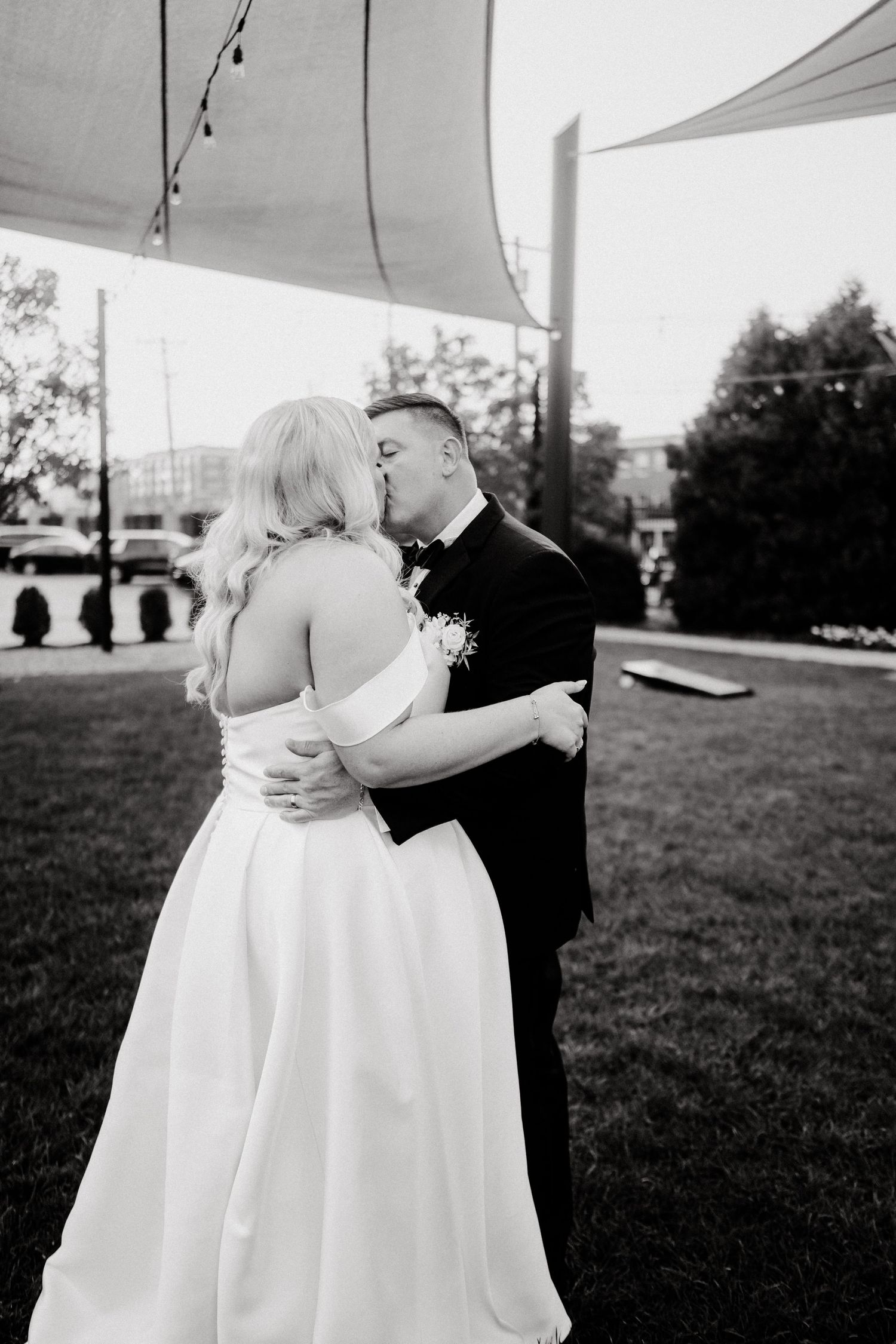 Black and white photo of a couple dancing outdoors under a tent at their wedding reception.