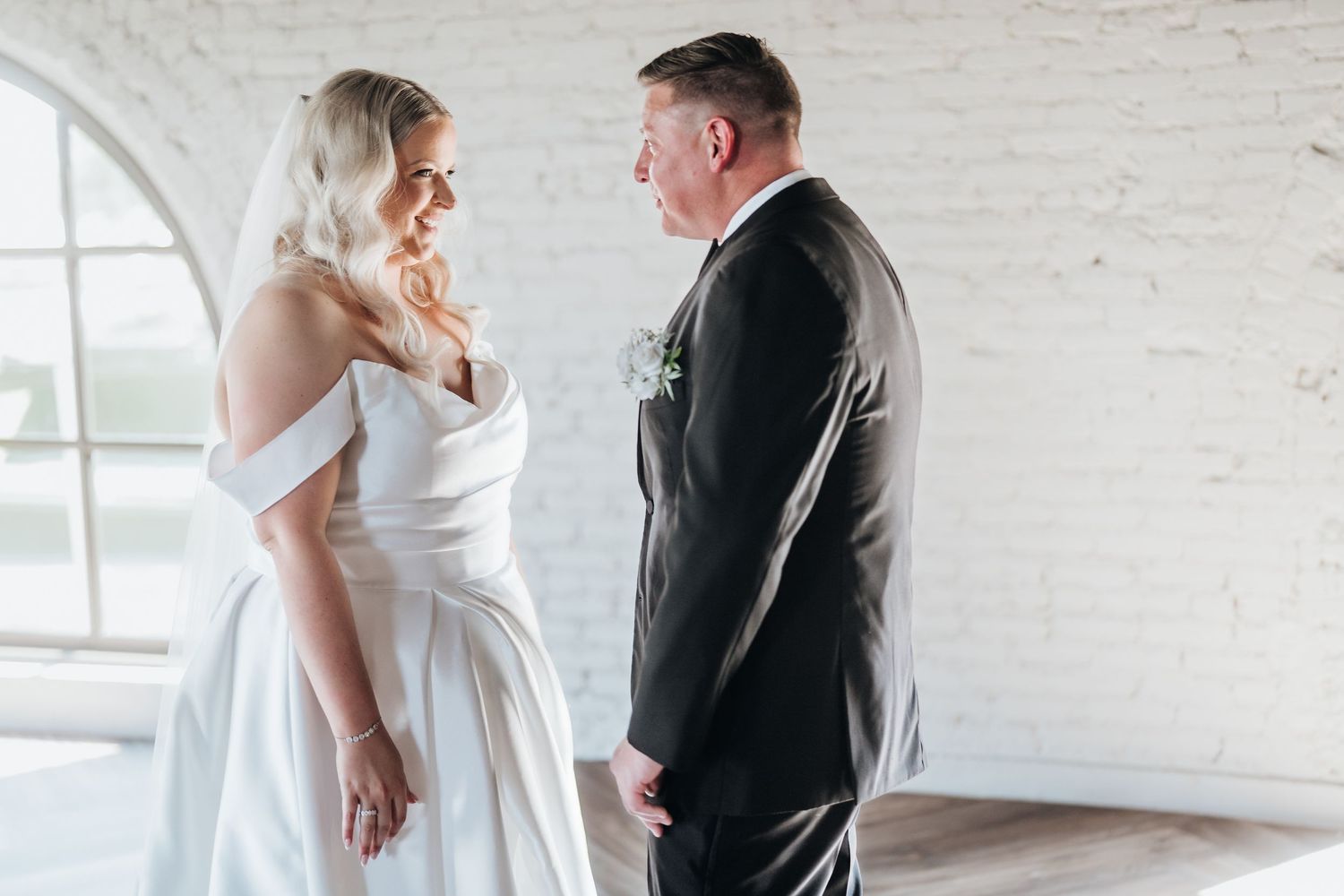 Intimate first look moment between bride and groom in a bright white industrial space.