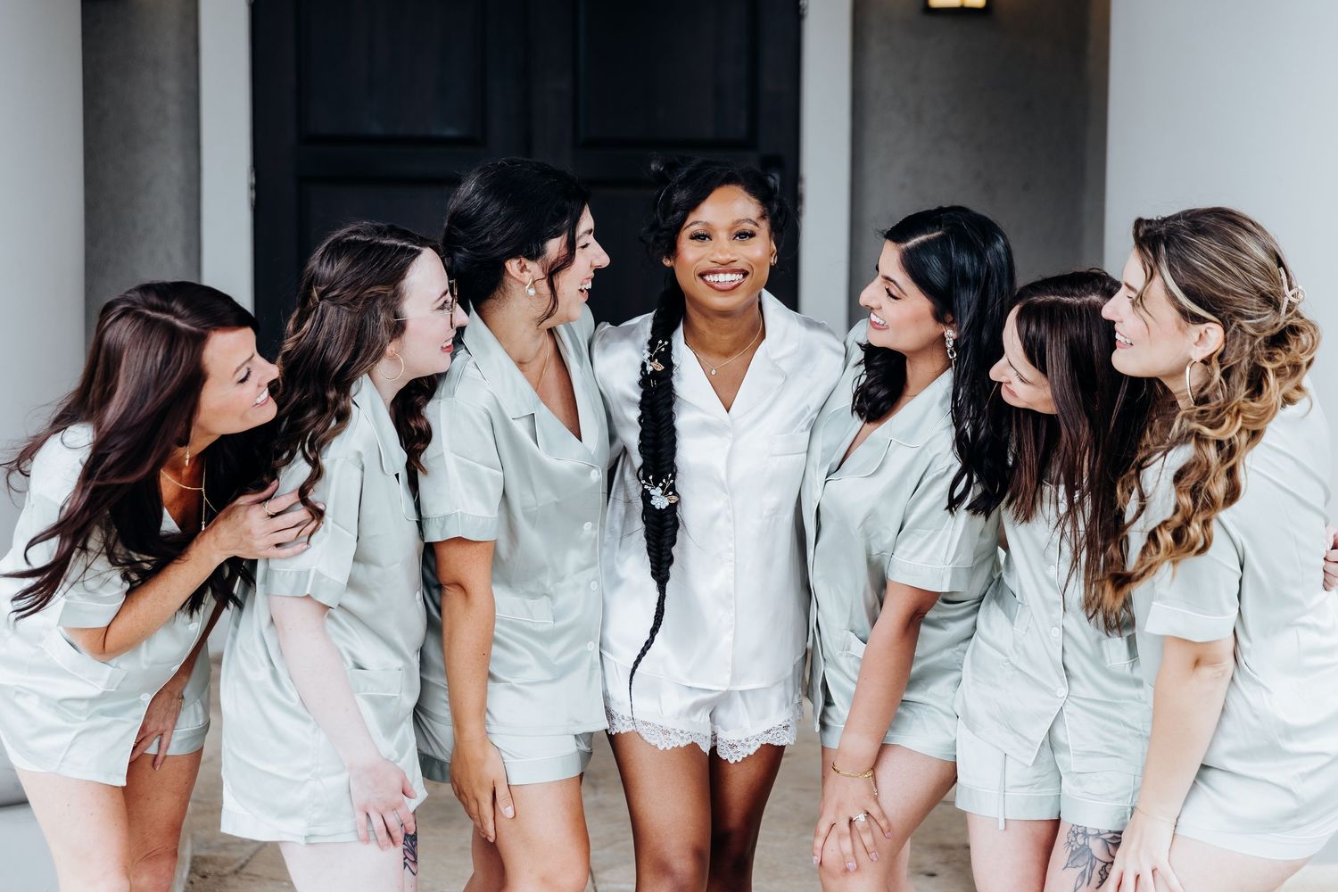 Row of bridesmaids in matching white robes posing together on a covered porch.