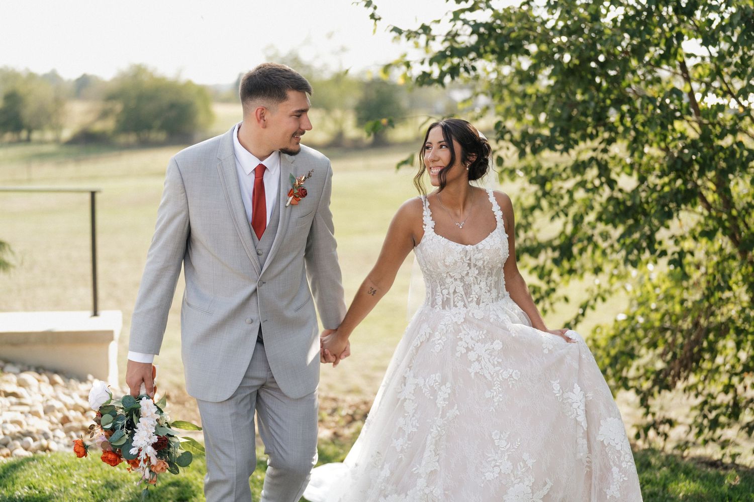 A couple walks hand in hand through a garden setting in wedding attire.