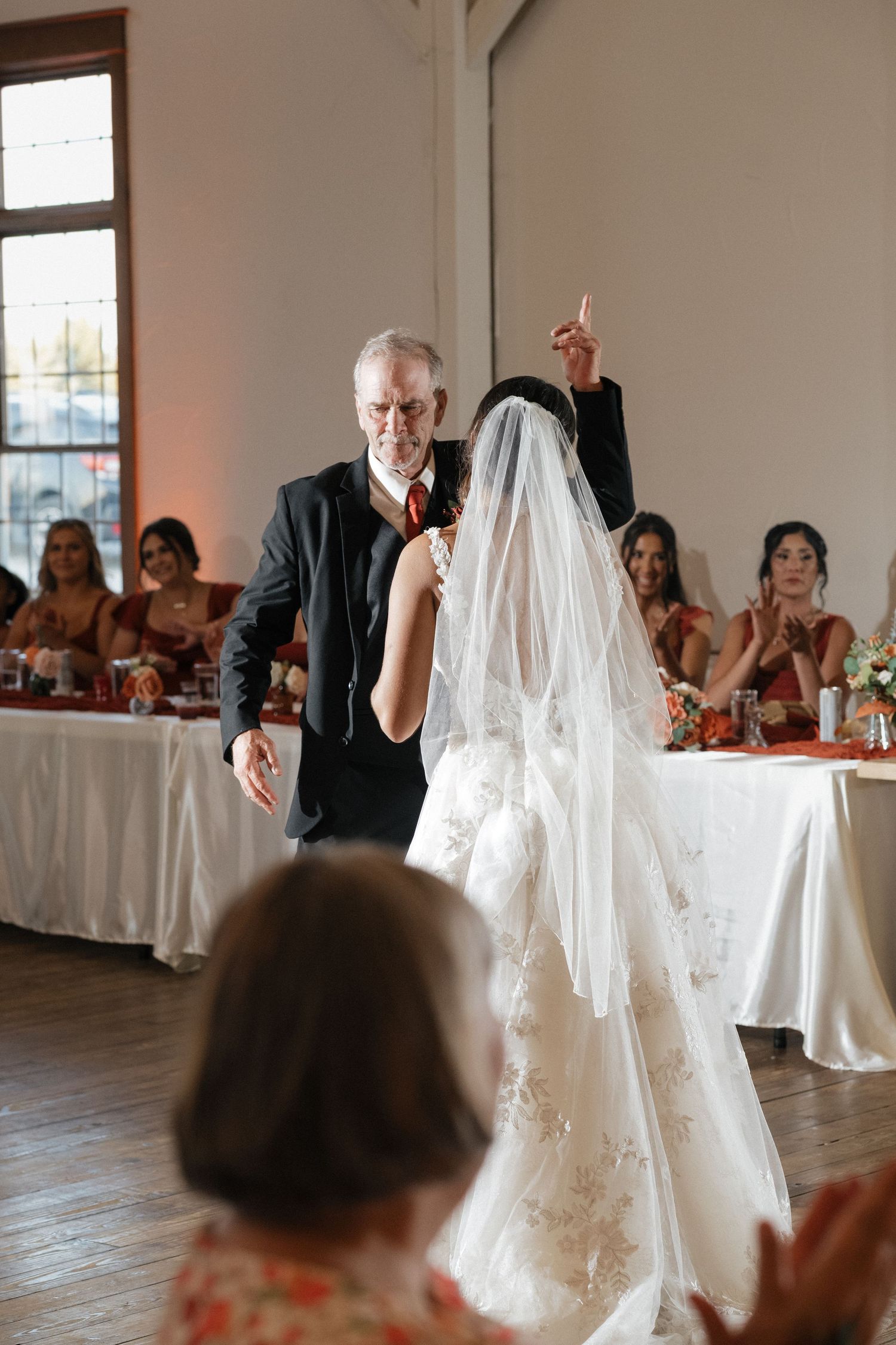 Wedding celebration in a bright indoor venue with guests seated at tables watching festivities.