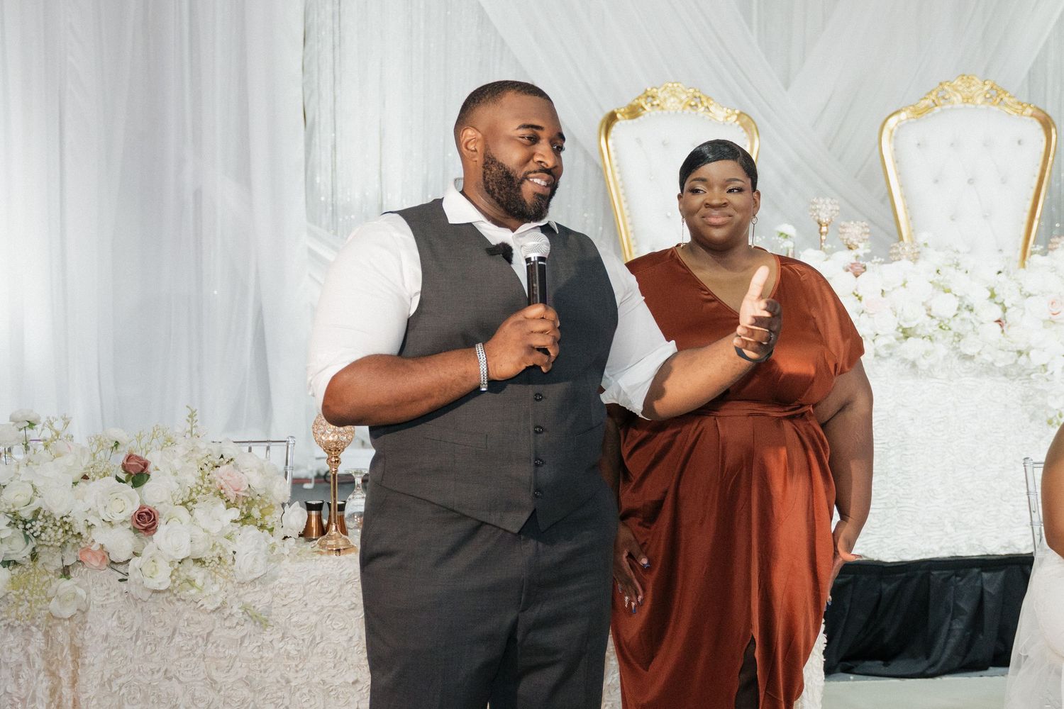 Wedding reception guests in formal attire pose together against an elegant white backdrop.