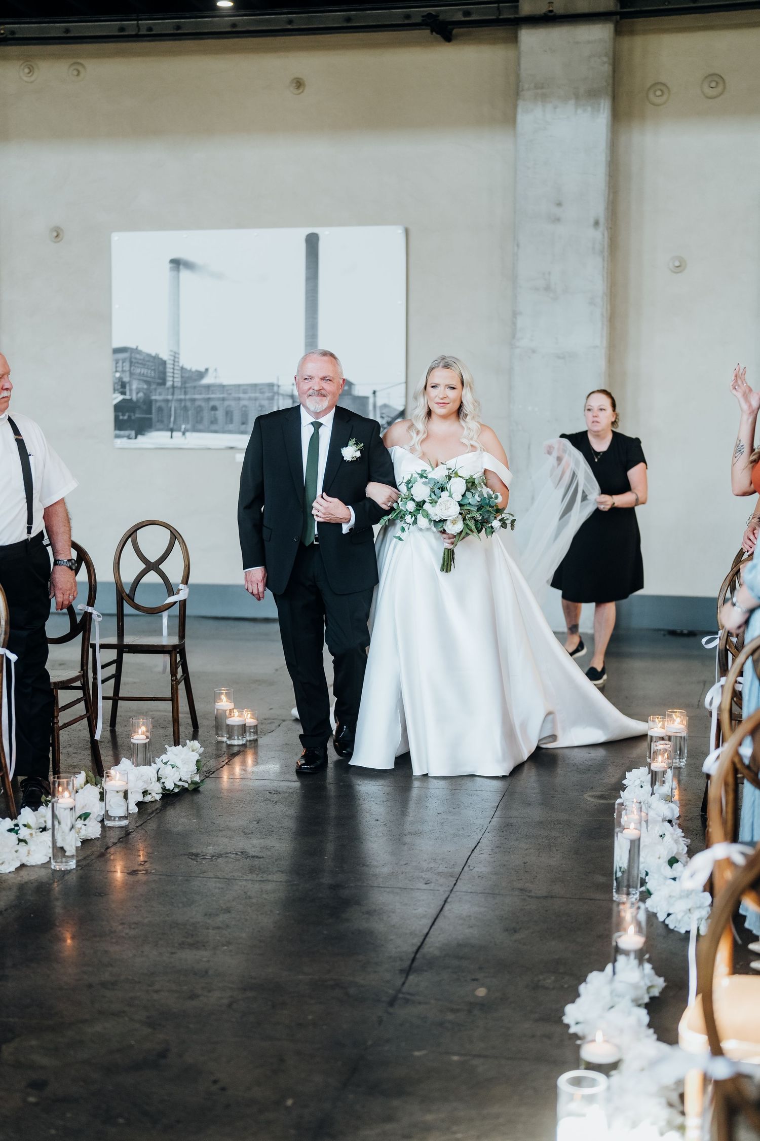 Wedding ceremony aisle decorated with candles and floral arrangements in an industrial venue.