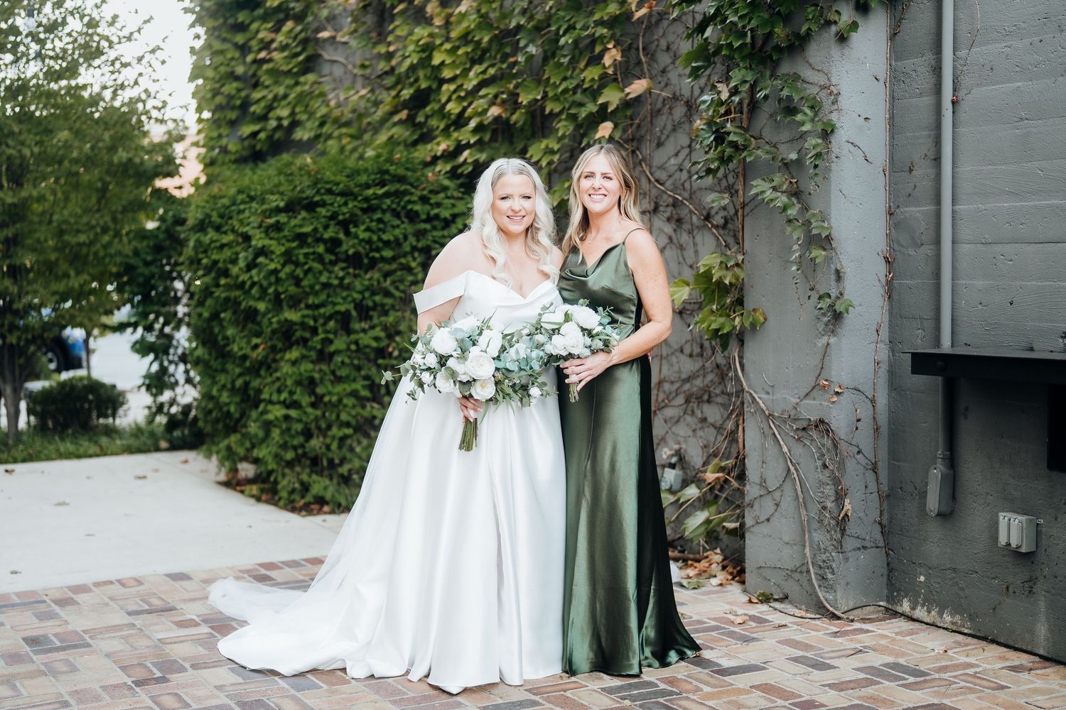 Wedding party poses outdoors against ivy-covered wall in sage green attire.