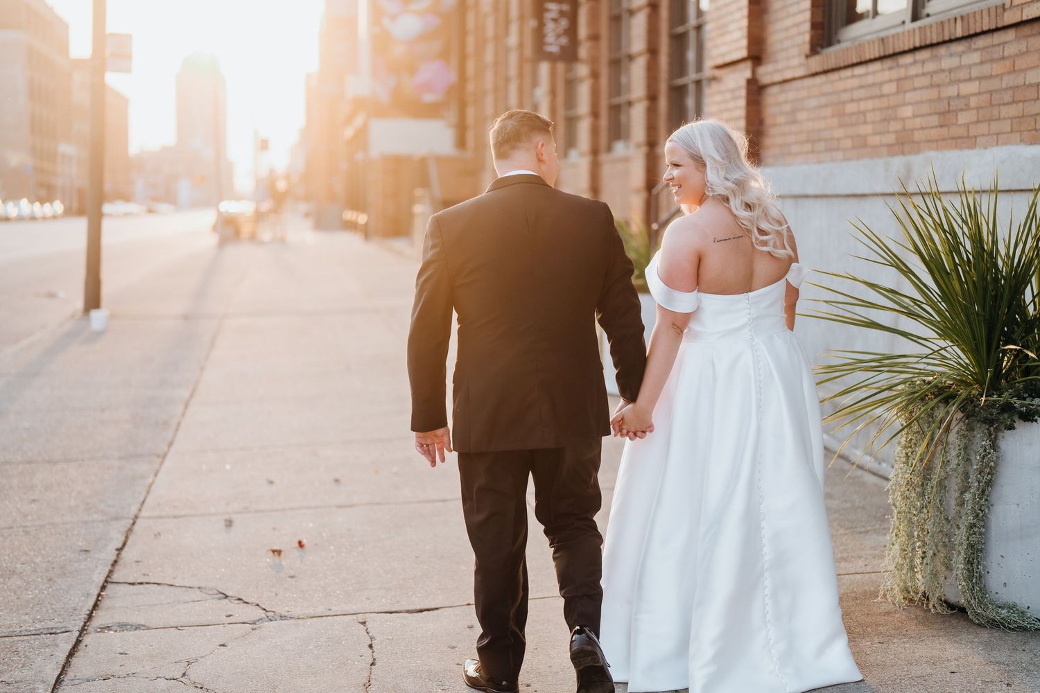 Newlyweds walking together on city sidewalk during golden hour sunset.