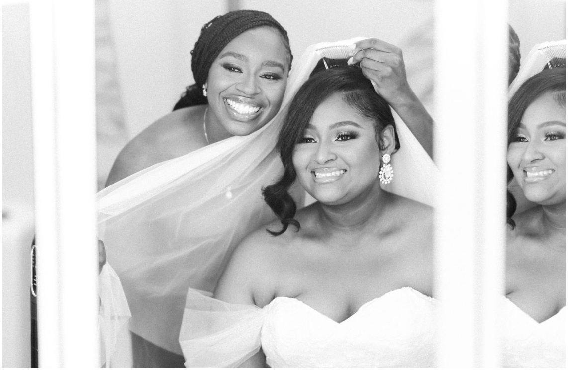 Three bridesmaids in white dresses share joyful moment while getting ready.