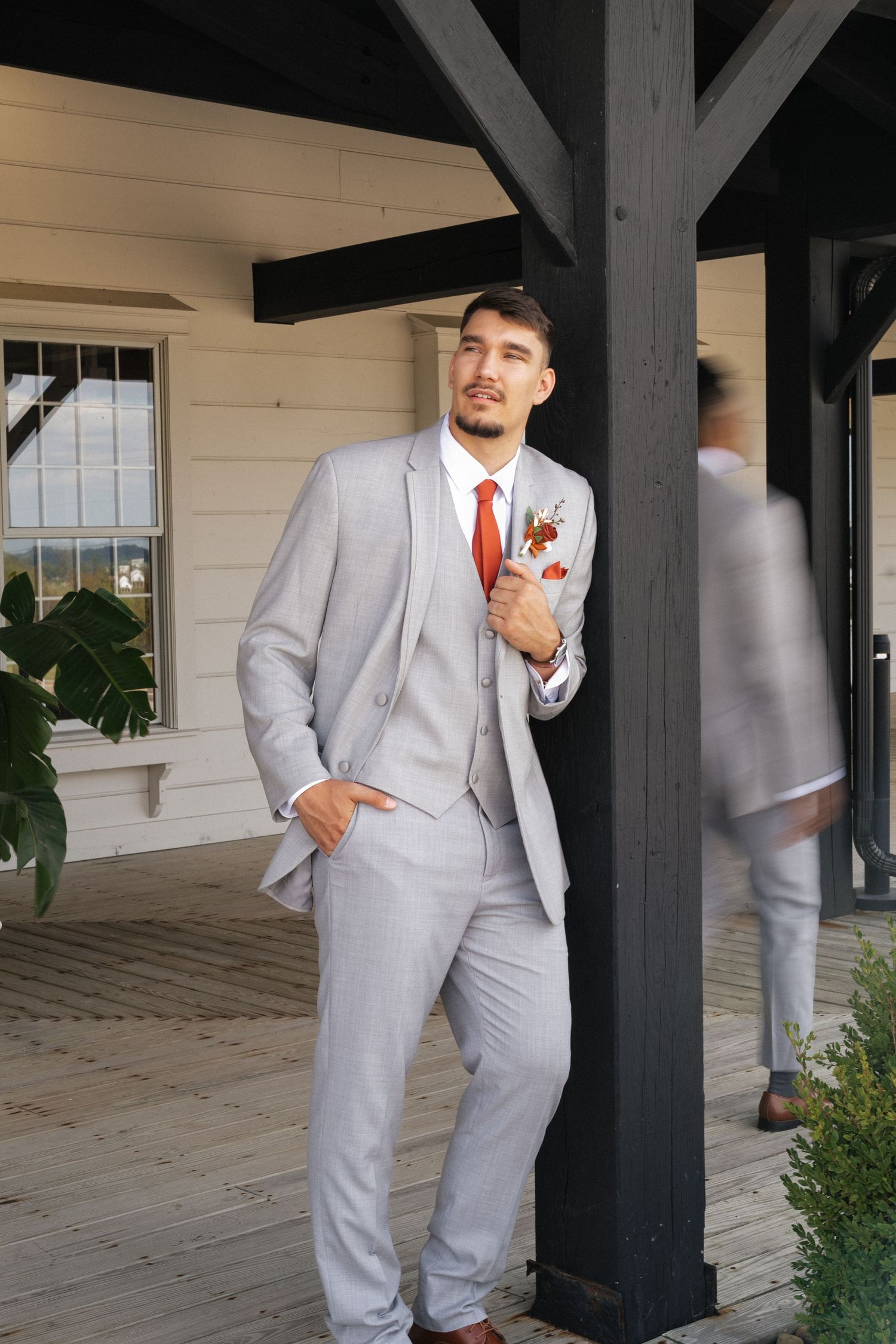 Wedding party members in gray suits relaxing under covered porch with black beams.