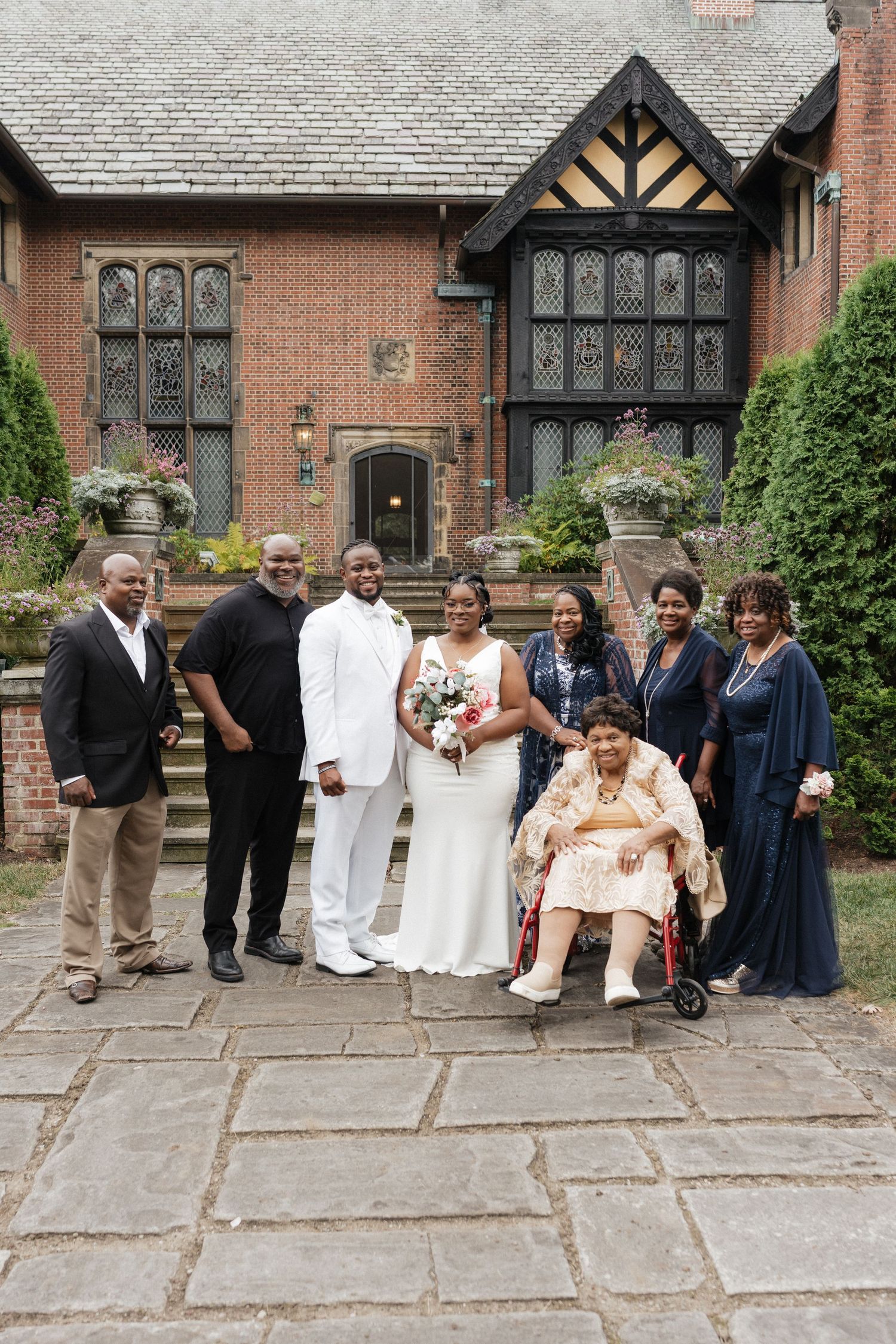 Wedding party poses in front of a Tudor-style brick mansion with ornate windows.