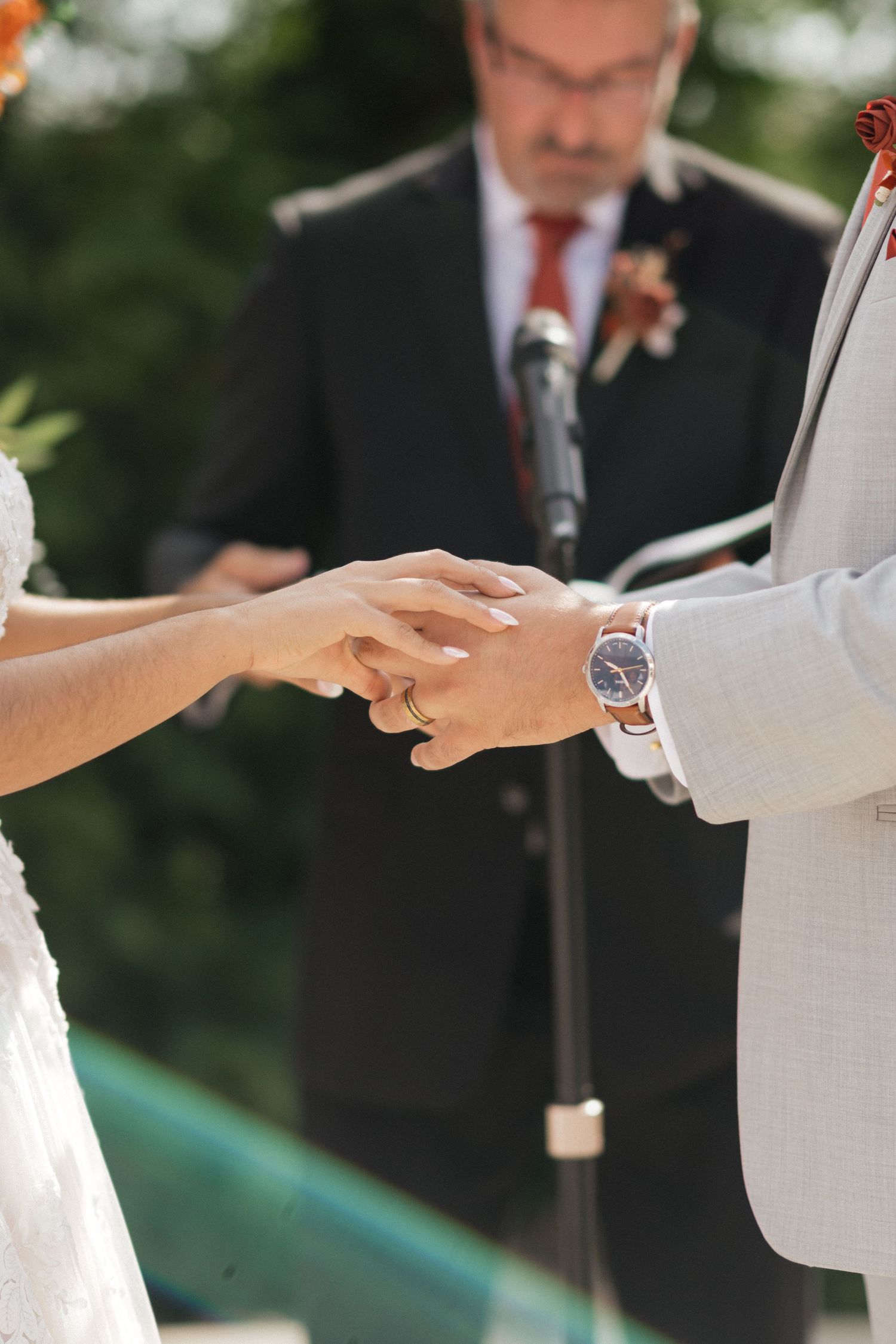 Close up of hands exchanging wedding rings during outdoor ceremony.