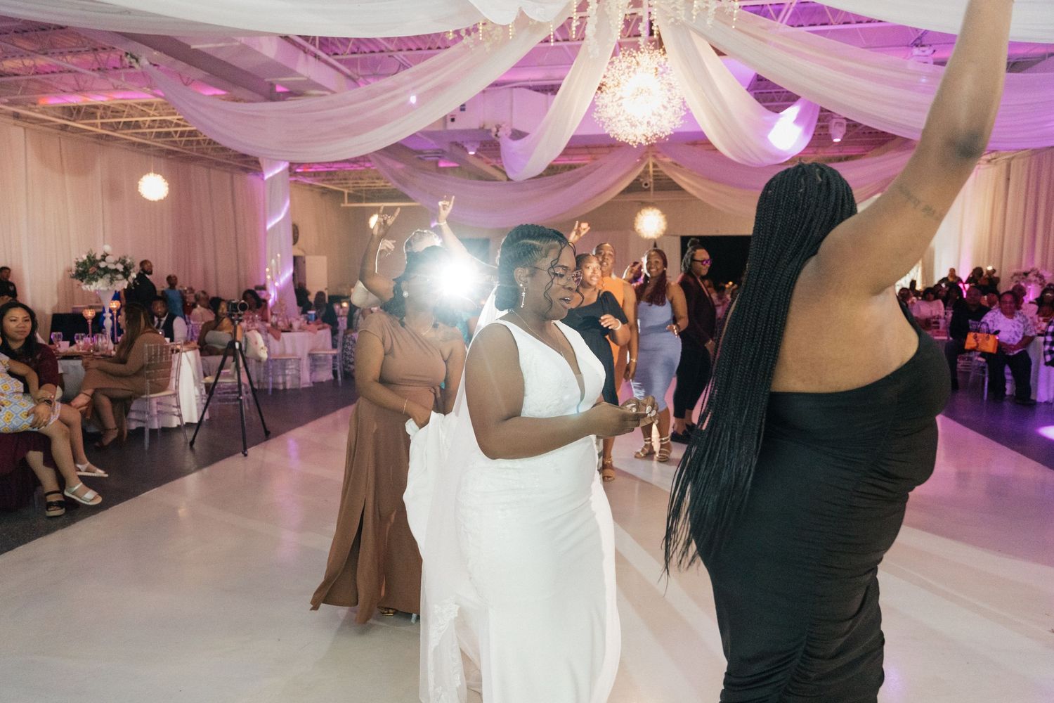 Wedding celebration with dancing and festivities in pink-lit reception venue.